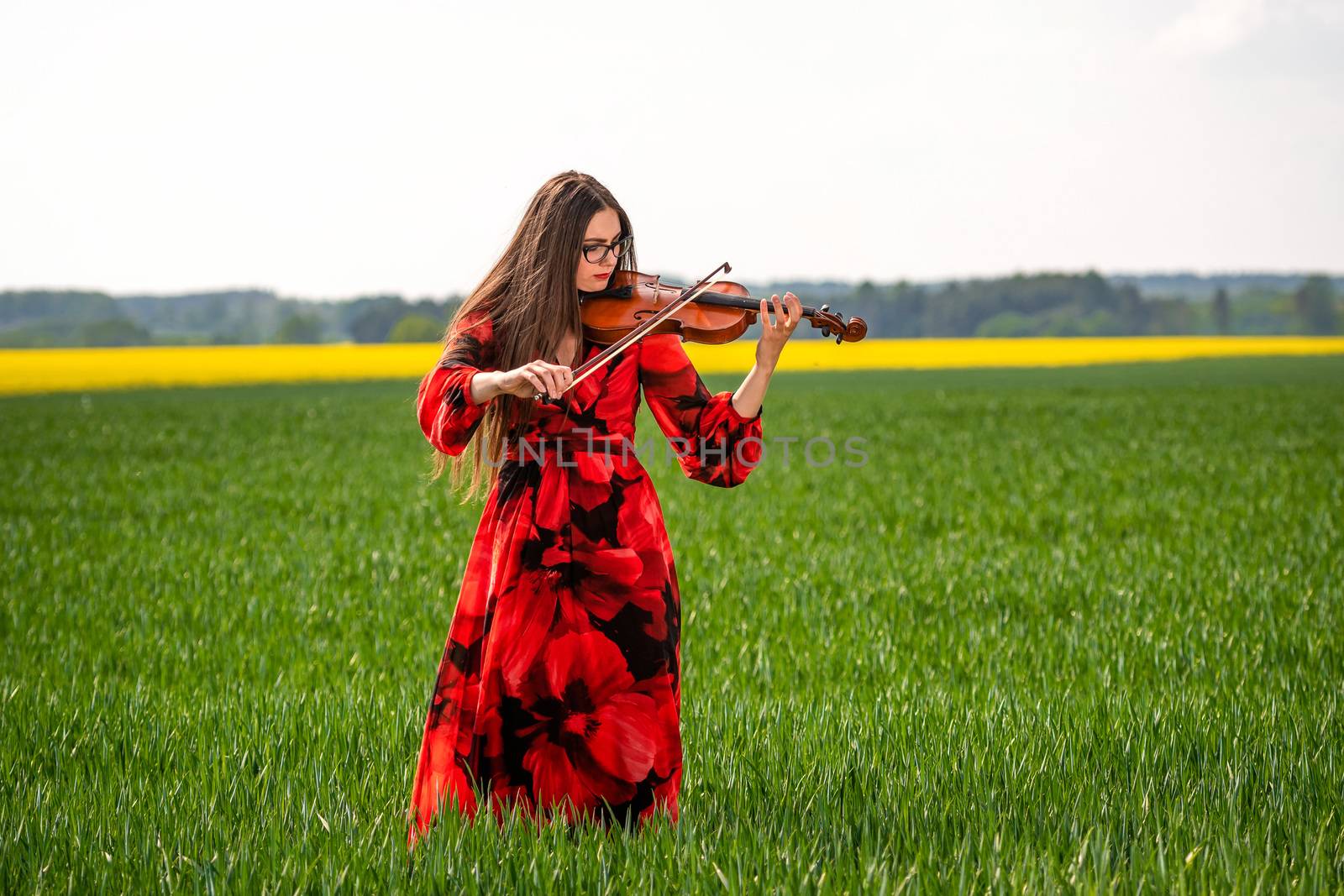 Young woman in red dress playing violin in green meadow.