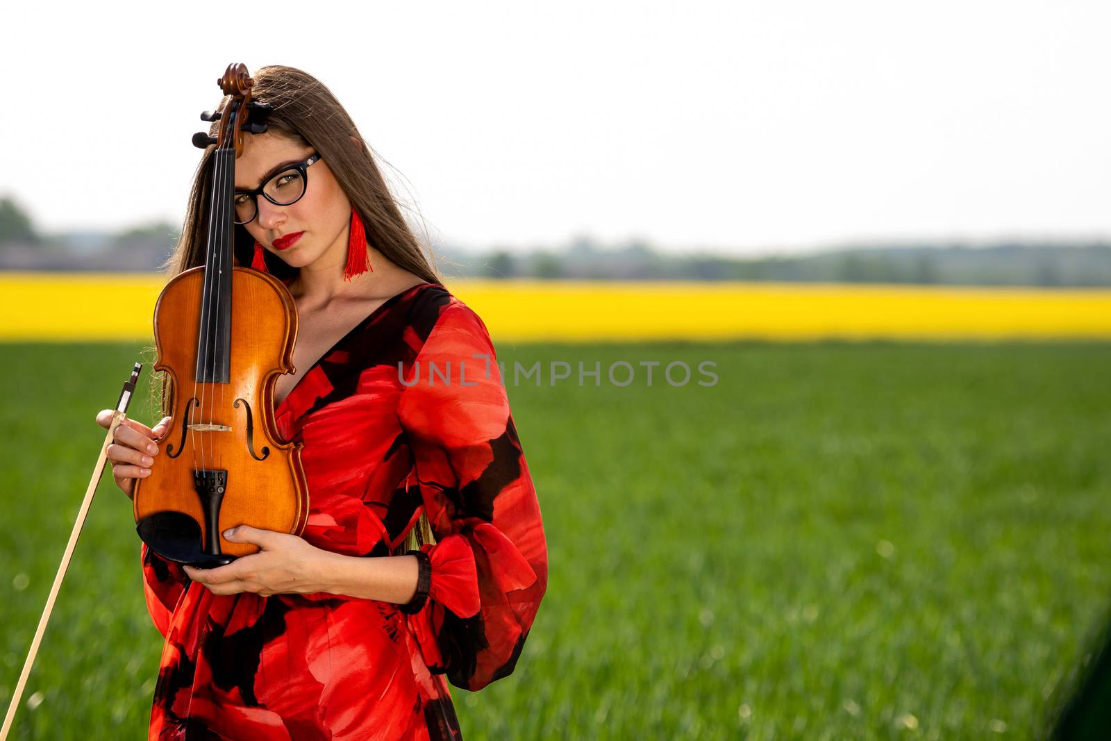 Young woman in red dress with violin in green meadow.