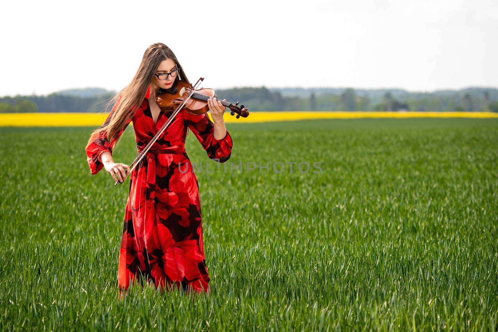 Young woman in red dress playing violin in green meadow.