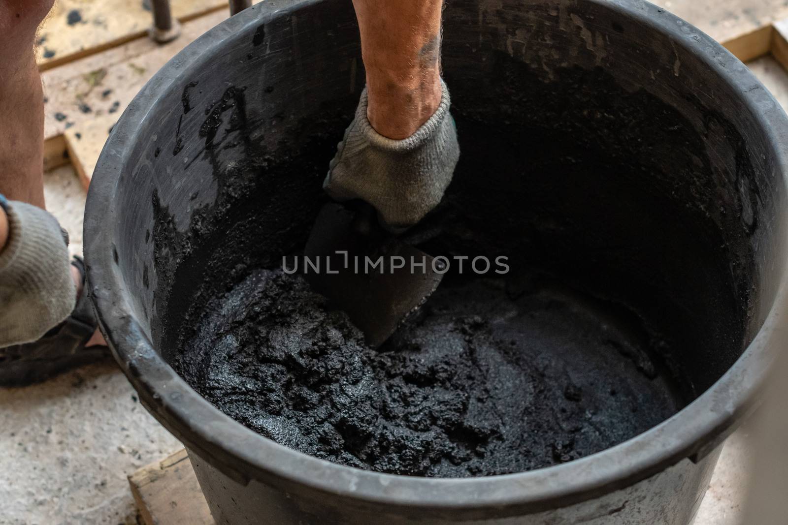 Mans hand hold a trowel and mixed cement in bucket.