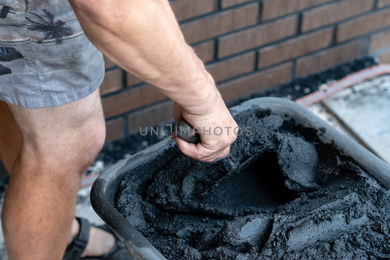 Mans hand hold a trowel and mixed cement in bucket.