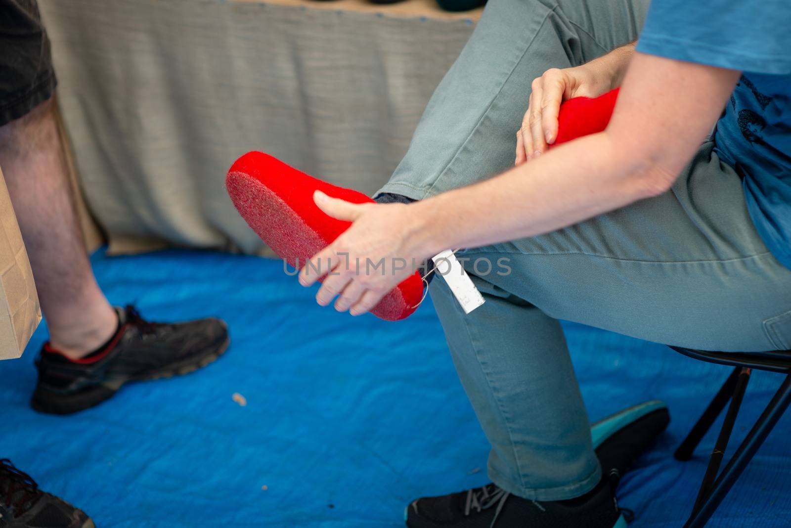 The man in the market measures red felt slippers. - image