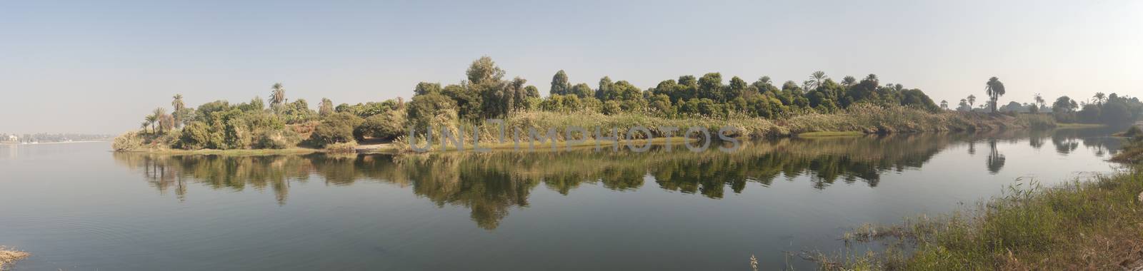 Vegetation along the banks of a large river with beautiful reflection and blue sky