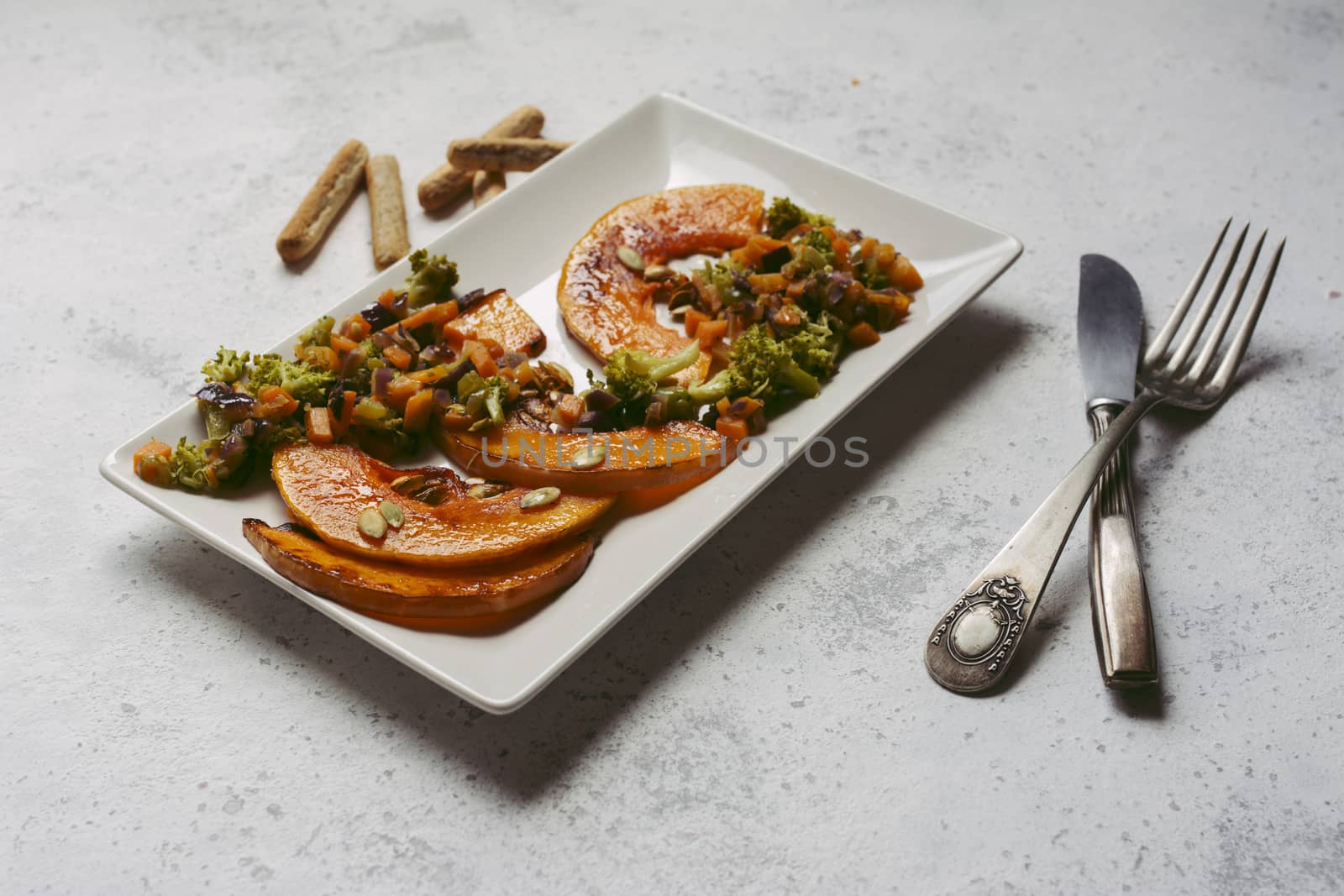 sliced baked pumpkin, with broccoli and assorted vegetables, on rectangular white plate