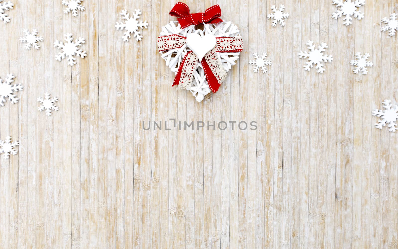 Flat lay shabby Christmas copy space with white wooden snowflakes and a white wooden decorative heart in the upper center side on light wooden background