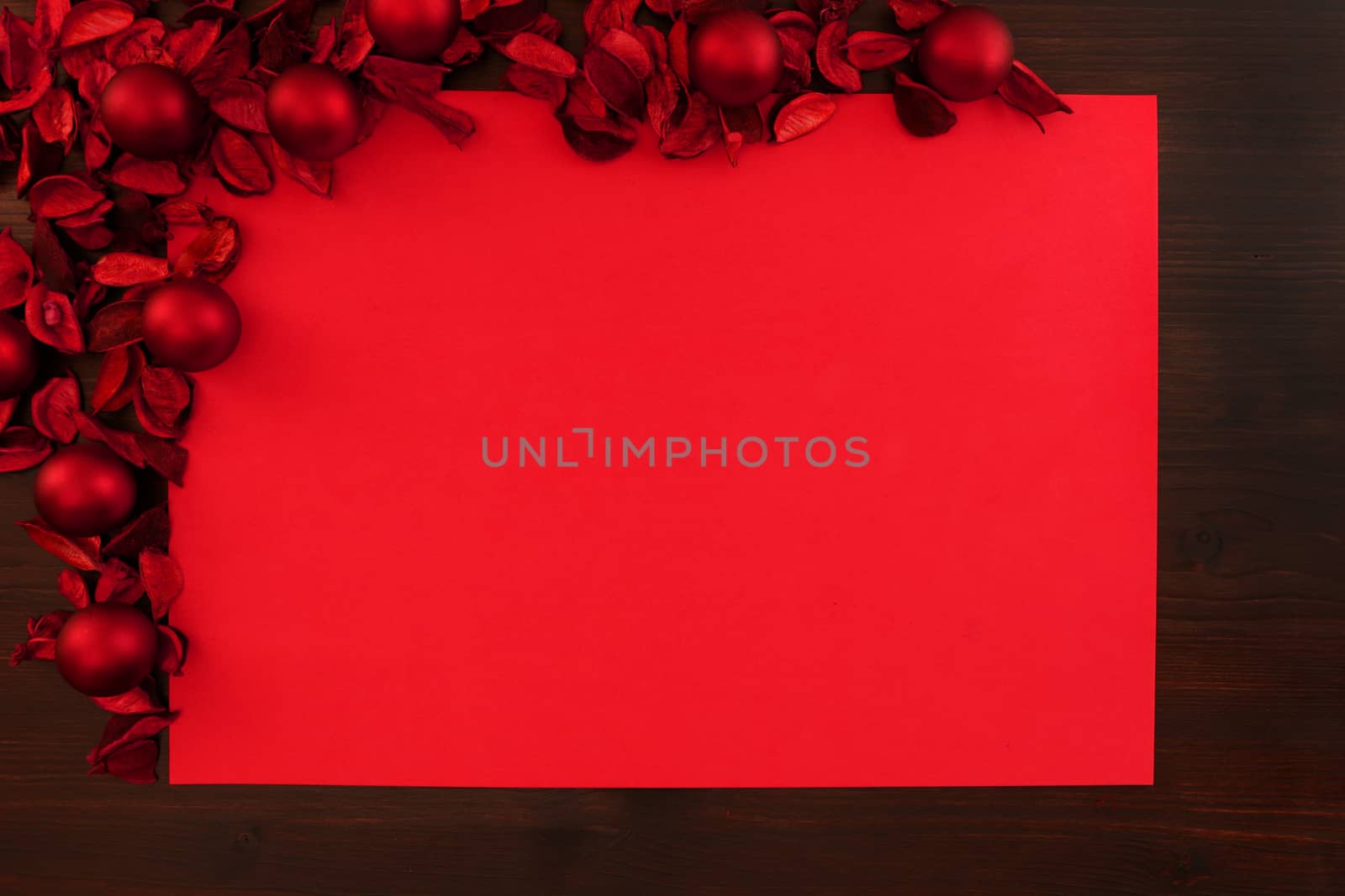 Flat lay red Christmas copy space with red petals and red Christmas balls in the upper left corner and dark wood all around