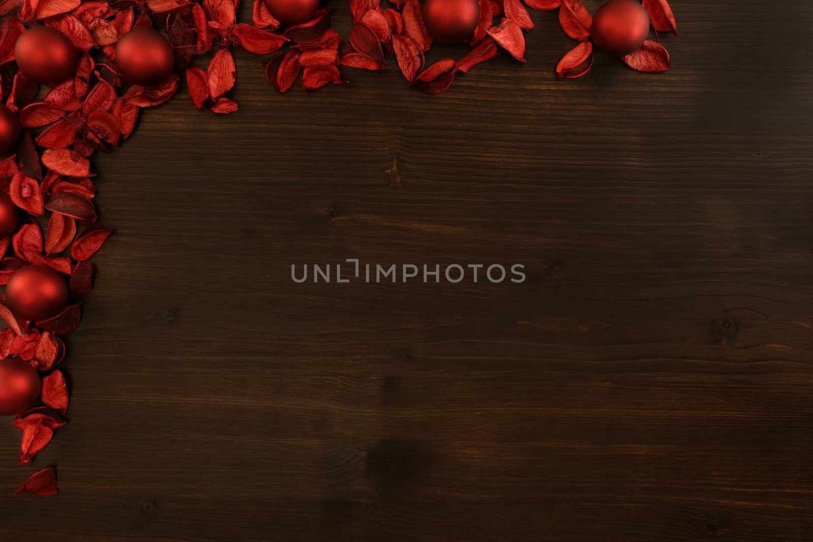 Flat lay dark wood Christmas copy space with red petals and red Christmas balls in the upper left corner by robbyfontanesi