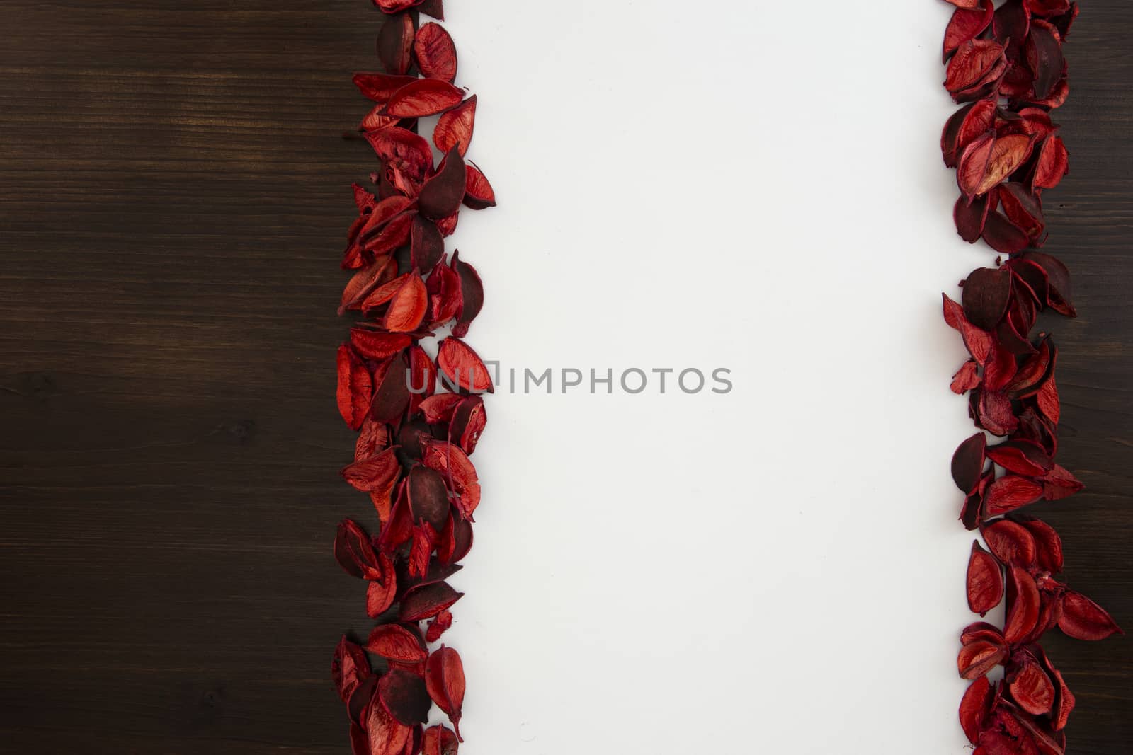 Flat lay Christmas copy space with dark wood on one side and red petals bordering a white background by robbyfontanesi