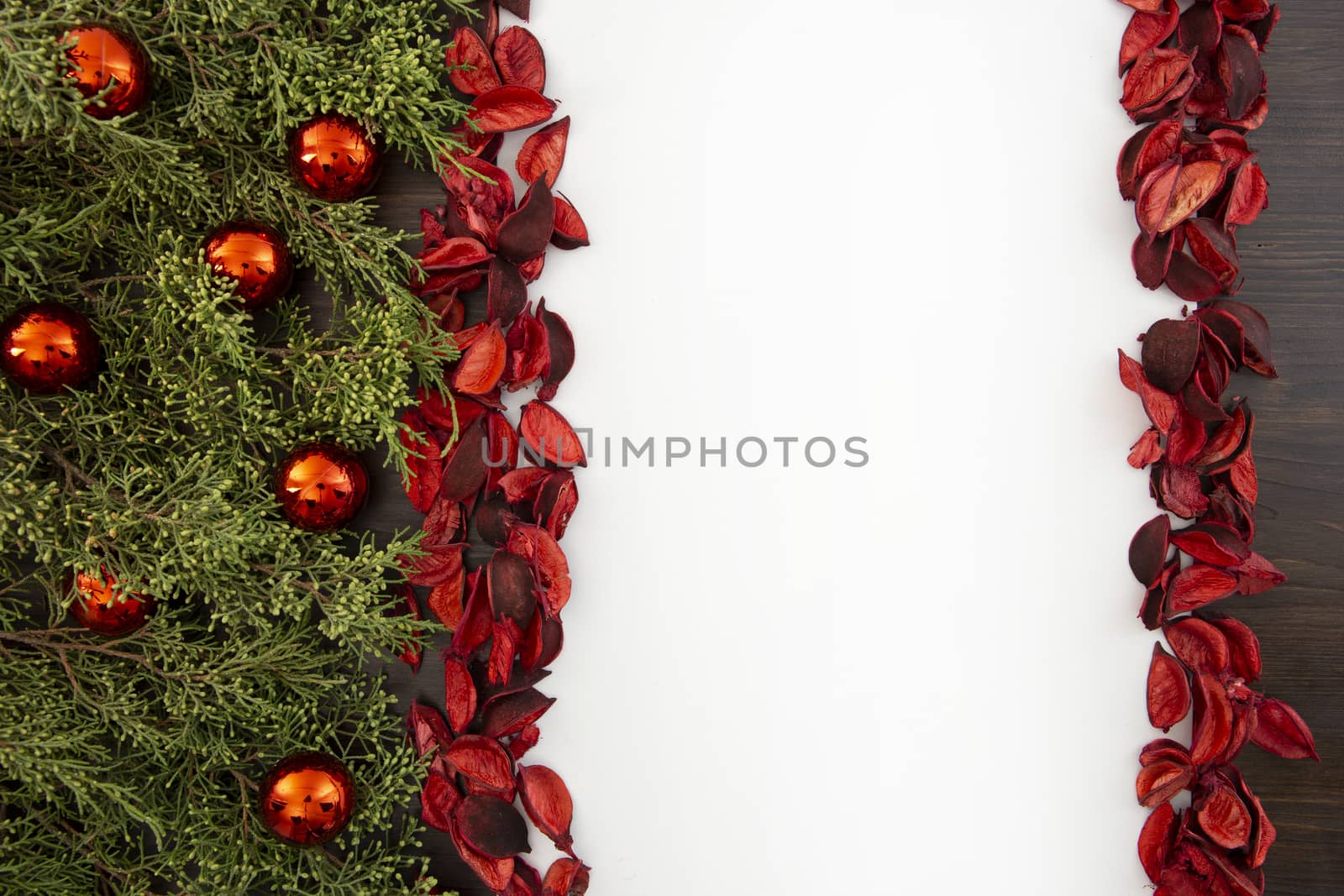 Flat lay Christmas copy space with pine branches, red Christmas baubles on one side and red petals bordering a white background