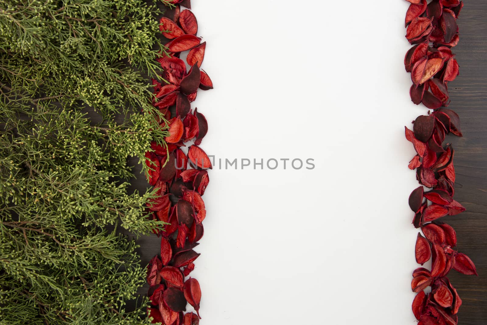 Flat lay Christmas copy space with pine branches on one side and red petals bordering a white background