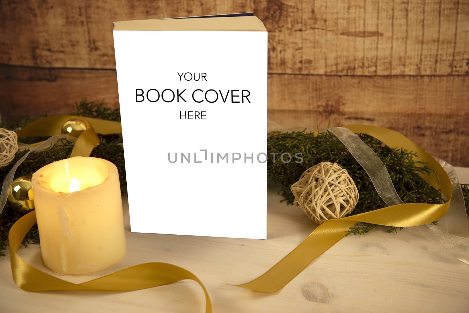 Christmas setting for a book presentation: book with blank cover settled with three lit candles , white organza and gold satin ribbons, gold baubles on light wooden table and dark wood background by robbyfontanesi