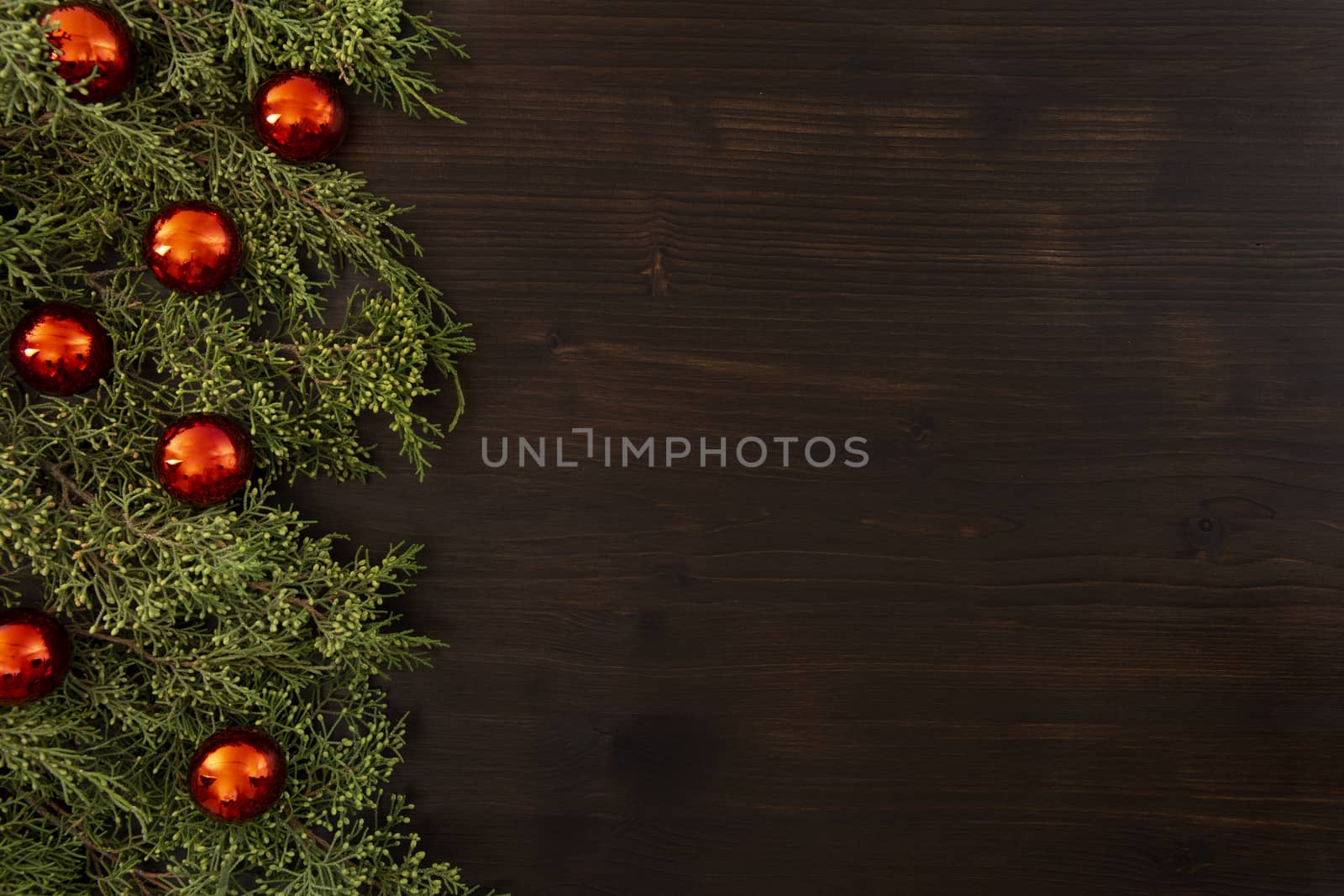 Flat lay Christmas copy space with pine branches and red Christmas baubles on a side on a dark wooden background