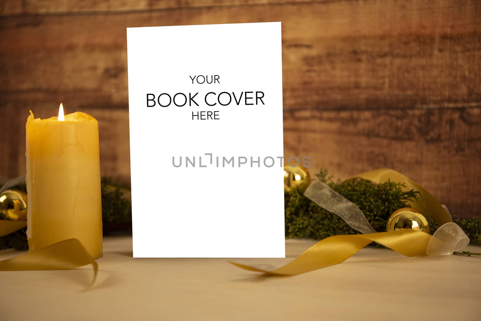 Christmas setting for a book presentation: book with blank cover settled with three lit candles , white organza and gold satin ribbons, gold baubles on light wooden table and dark wood background by robbyfontanesi