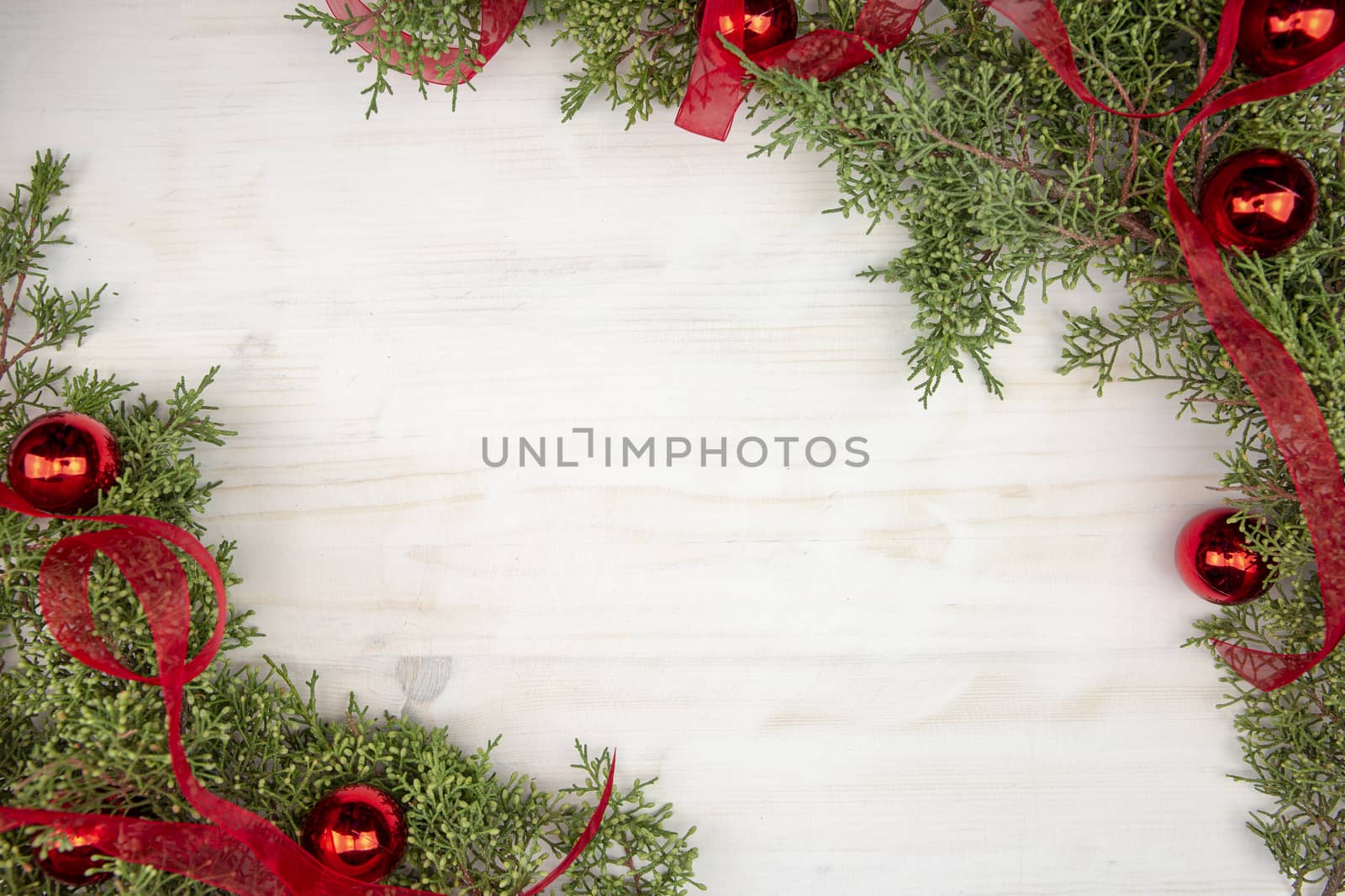 Flat lay Christmas copy space with pine branches, red organza ribbon and red Christmas baubles on a light wooden background