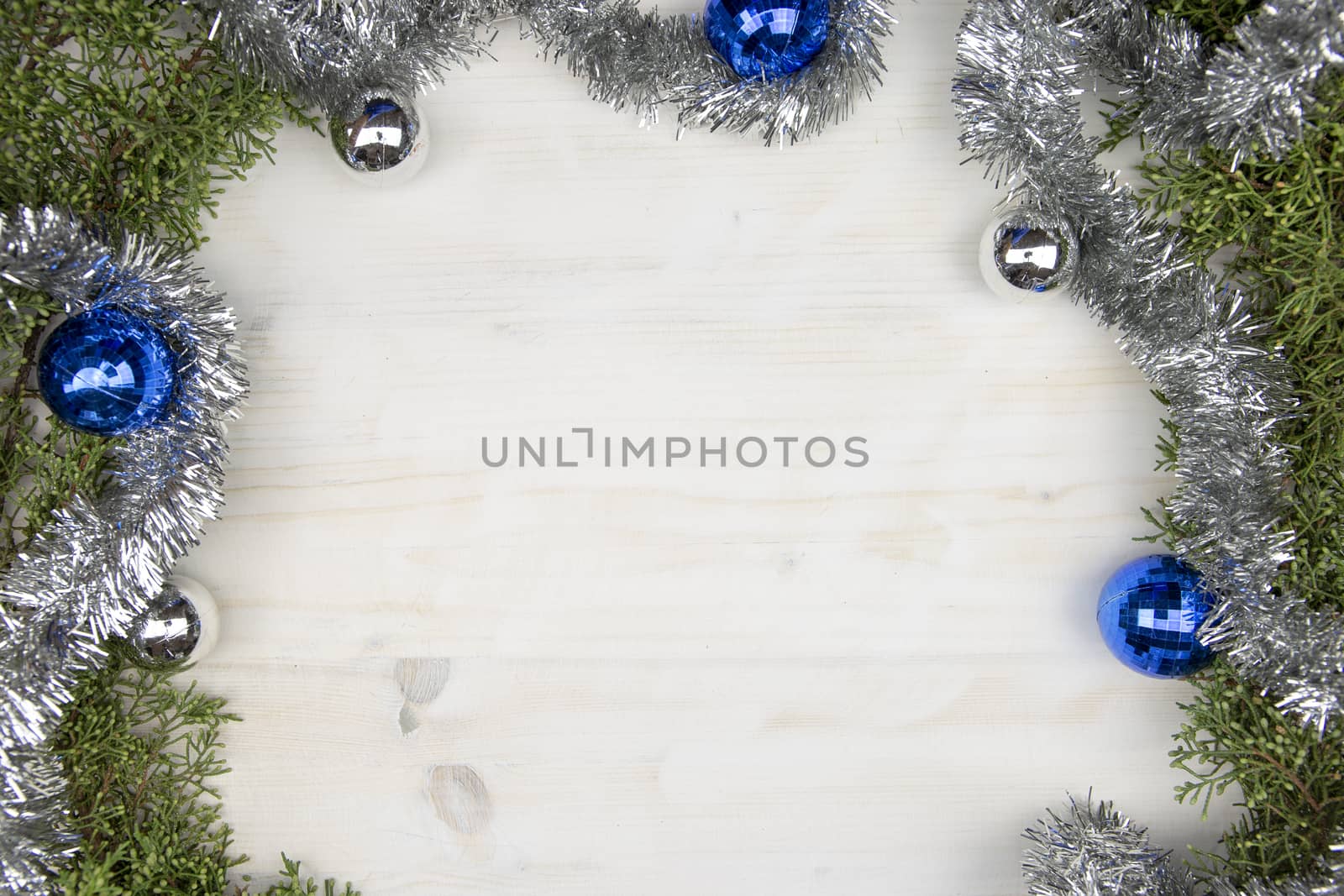 Flat lay Christmas space with pine branches, silver garland and silver and blue Christmas baubles on a light wooden background by robbyfontanesi