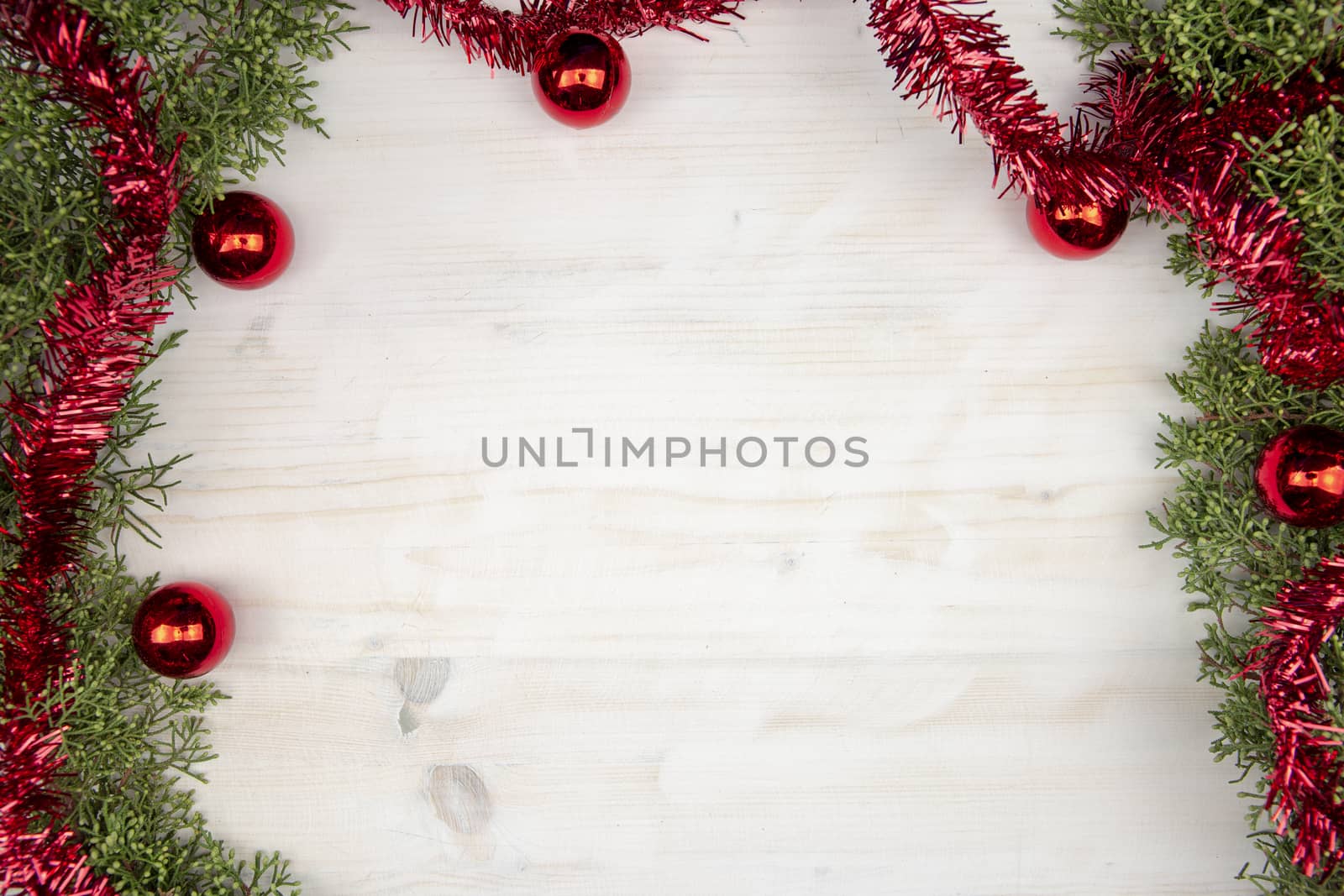 Flat lay Christmas copy space with pine branches, red garland and red Christmas baubles on a light wooden background by robbyfontanesi