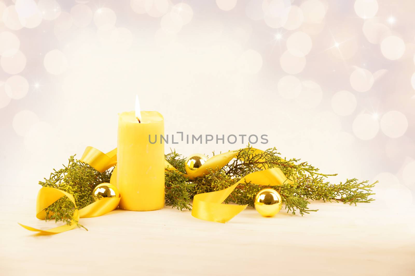 Christmas copy space with a lit yellow candle, pine branches, golden satin ribbon and gold-colored Christmas balls on a light patterned background by robbyfontanesi