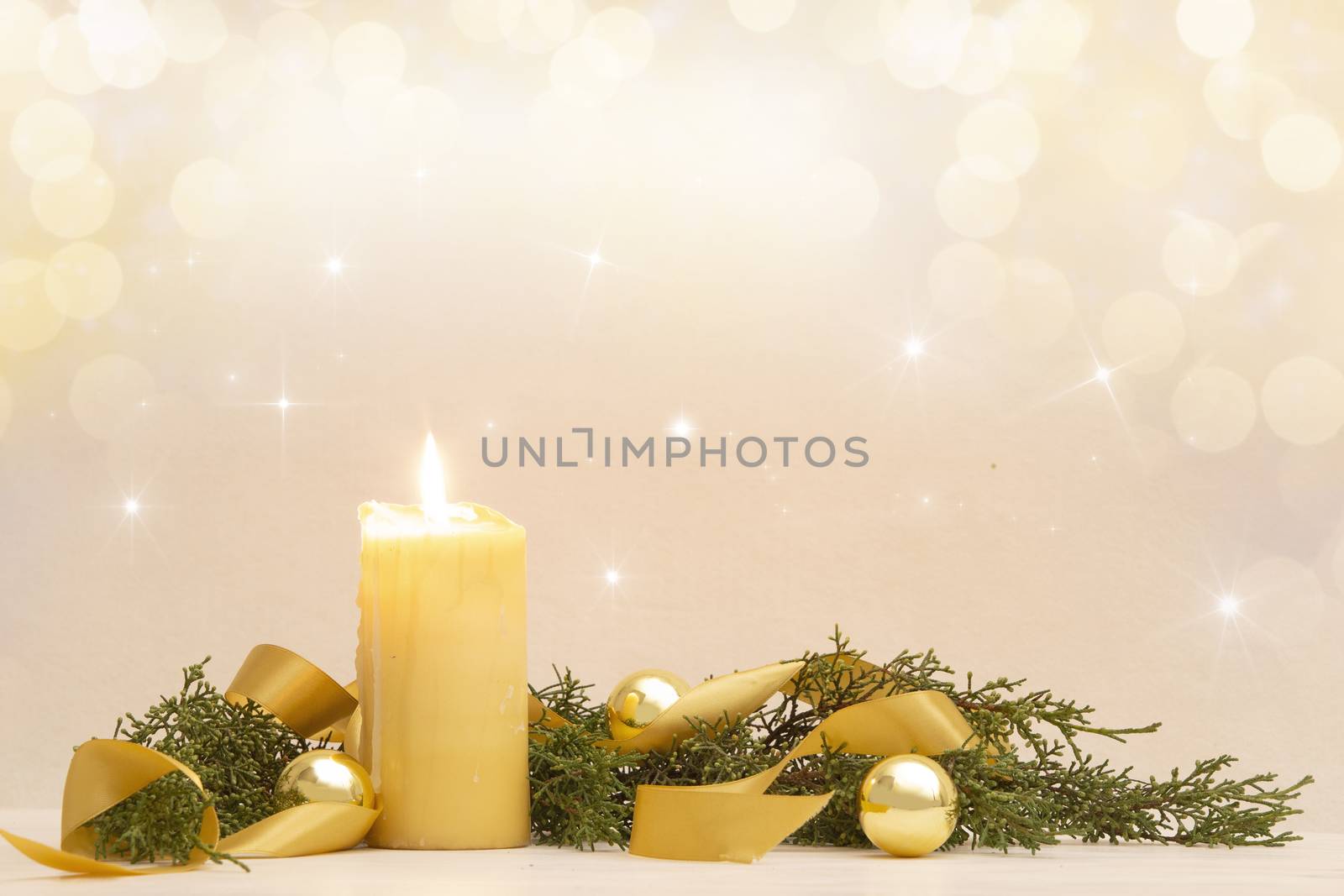 Christmas copy space with a lit yellow candle, pine branches, golden satin ribbon and gold-colored Christmas balls on a light patterned background