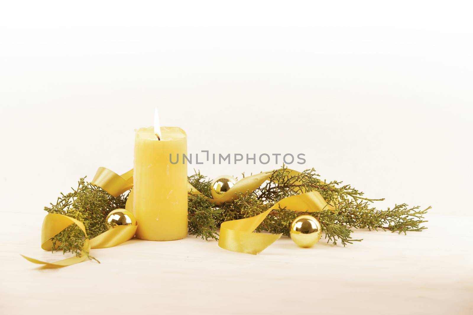 Christmas copy space with a lit yellow candle, pine branches, golden satin ribbon and gold-colored Christmas balls on a light patterned background by robbyfontanesi