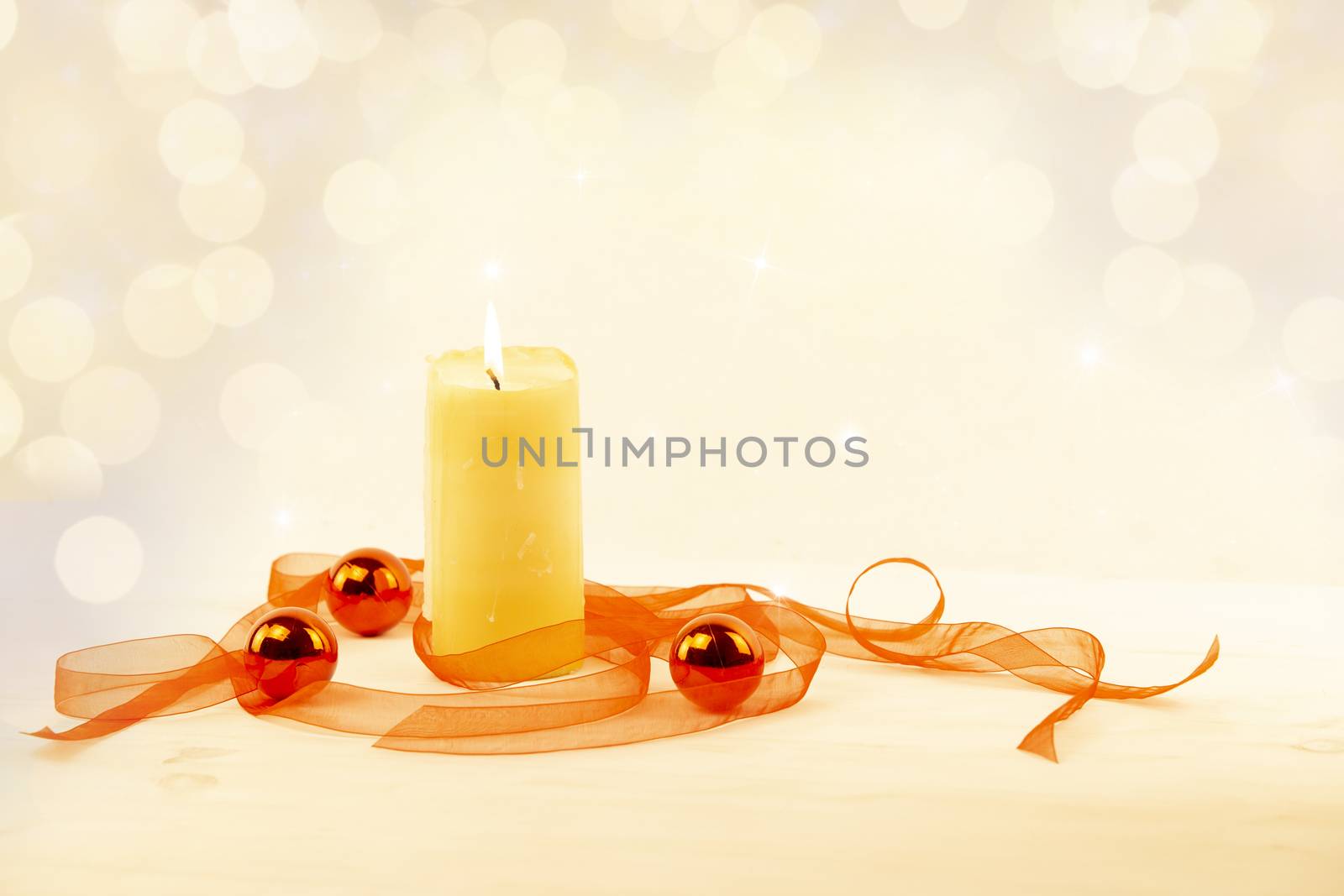 Christmas copy space with a lit yellow candle, red organza ribbon and red Christmas balls on a light patterned background