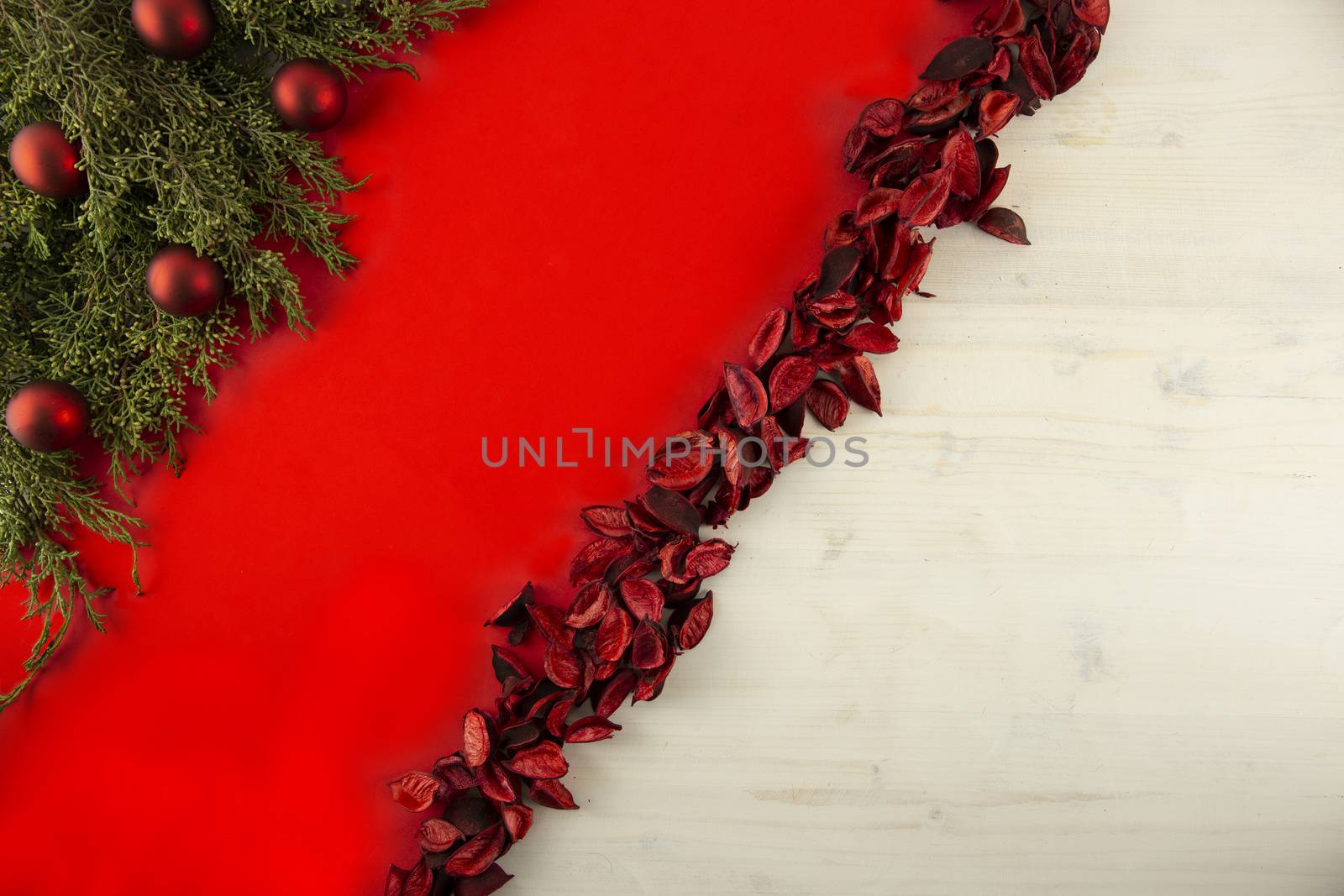 Flat lay red Christmas copy space with a diagonal red stripe on light wooden background, pine branches, red petals and red Christmas baubles