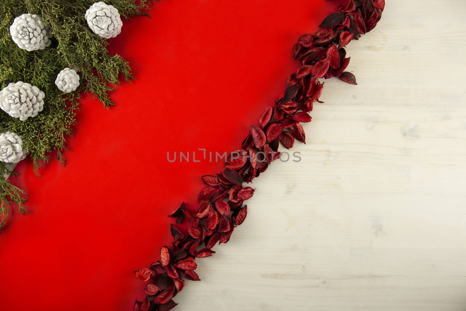 Flat lay red Christmas copy space with a diagonal red stripe on light wooden background, pine branches, white pine cones and red petals