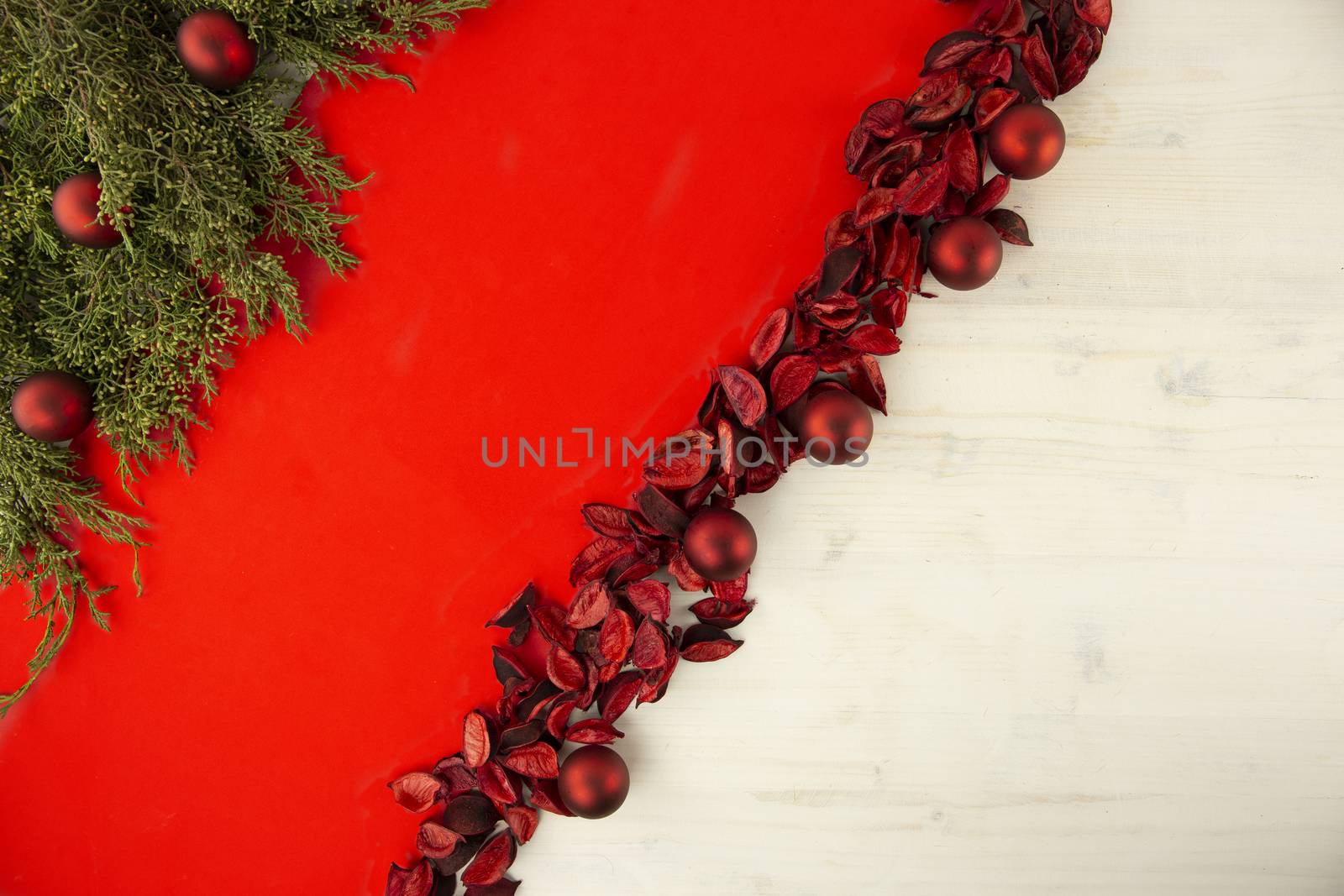 Flat lay red Christmas copy space with a diagonal red stripe on light wooden background, pine branches, red petals and red Christmas baubles