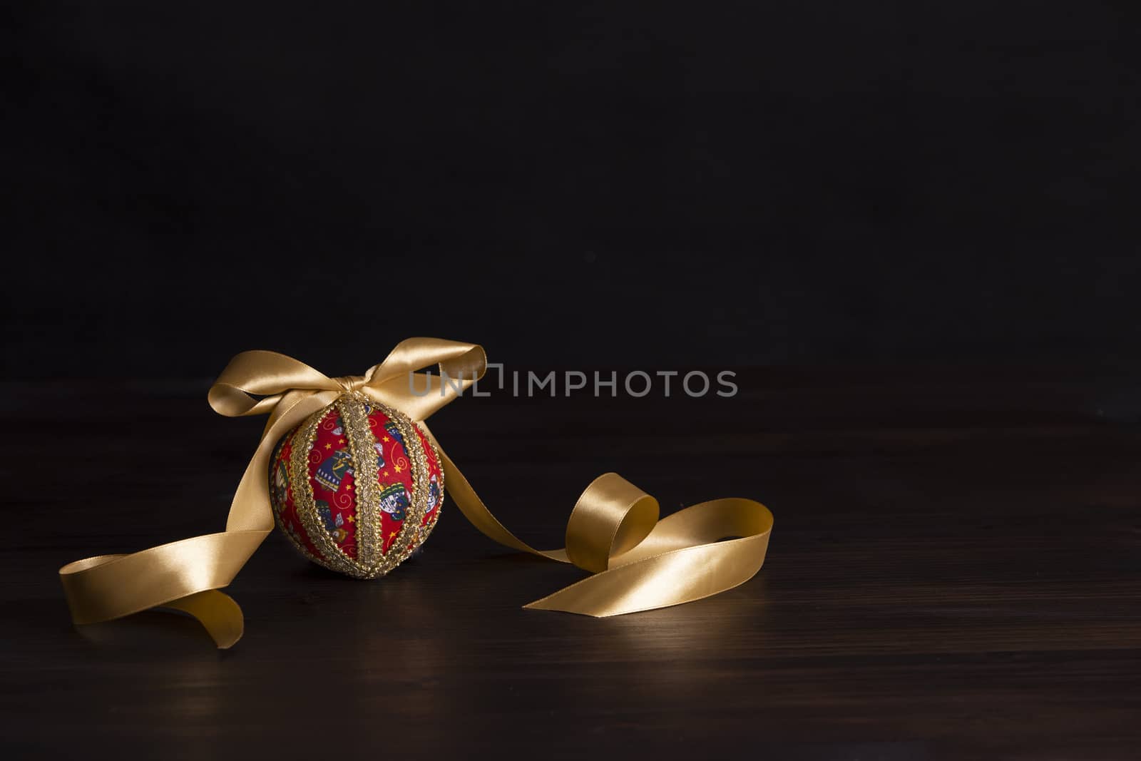 Dark wood Christmas copy space: decoupage christmas isolated ball close up with gold satin ribbon in black background by robbyfontanesi