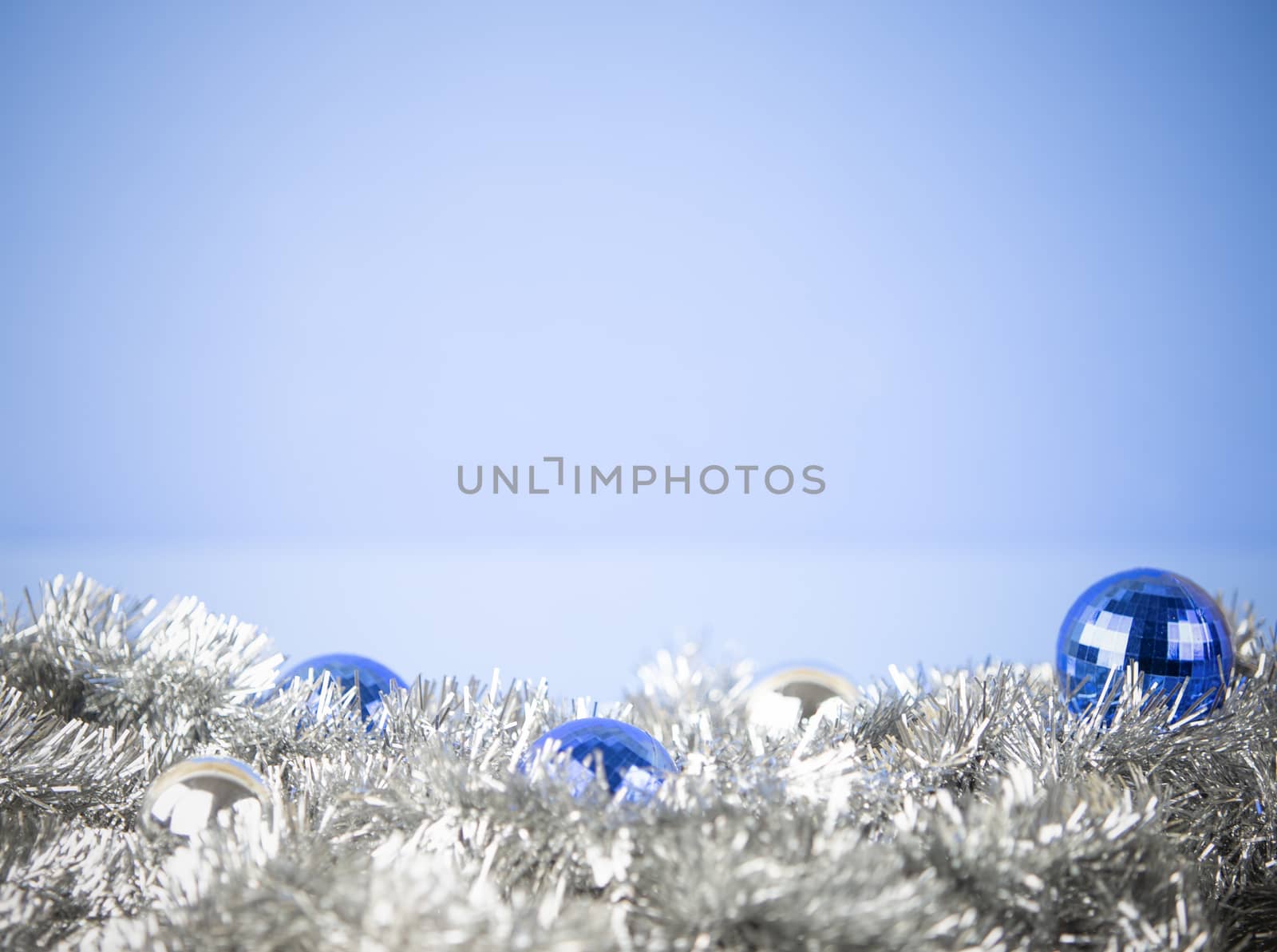 Christmas copy space with blue and silver bright baubles in silver decorative chain garland on light blue background with bokeh effect