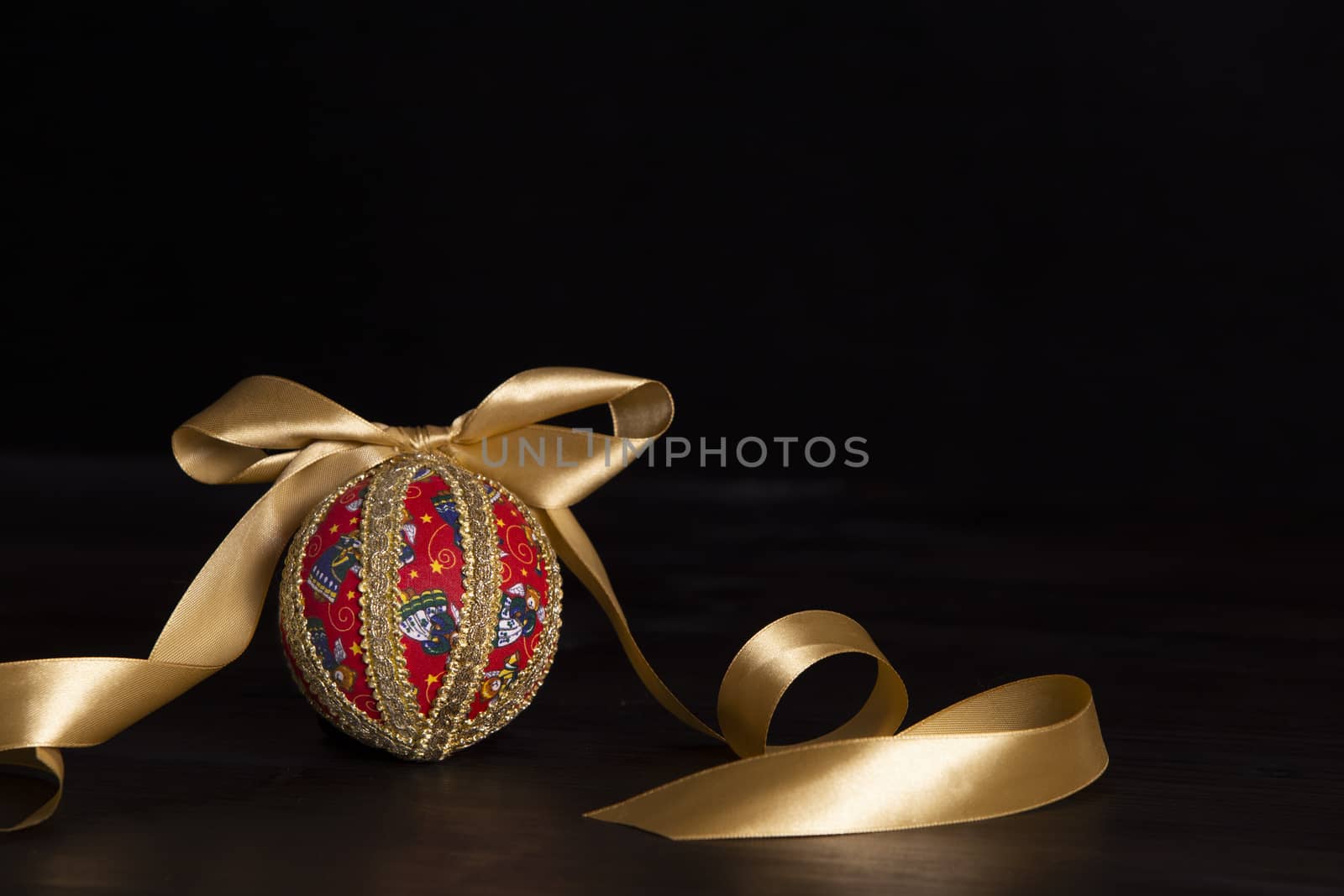 Dark wood Christmas copy space: decoupage christmas isolated ball close up with gold satin ribbon in black background by robbyfontanesi