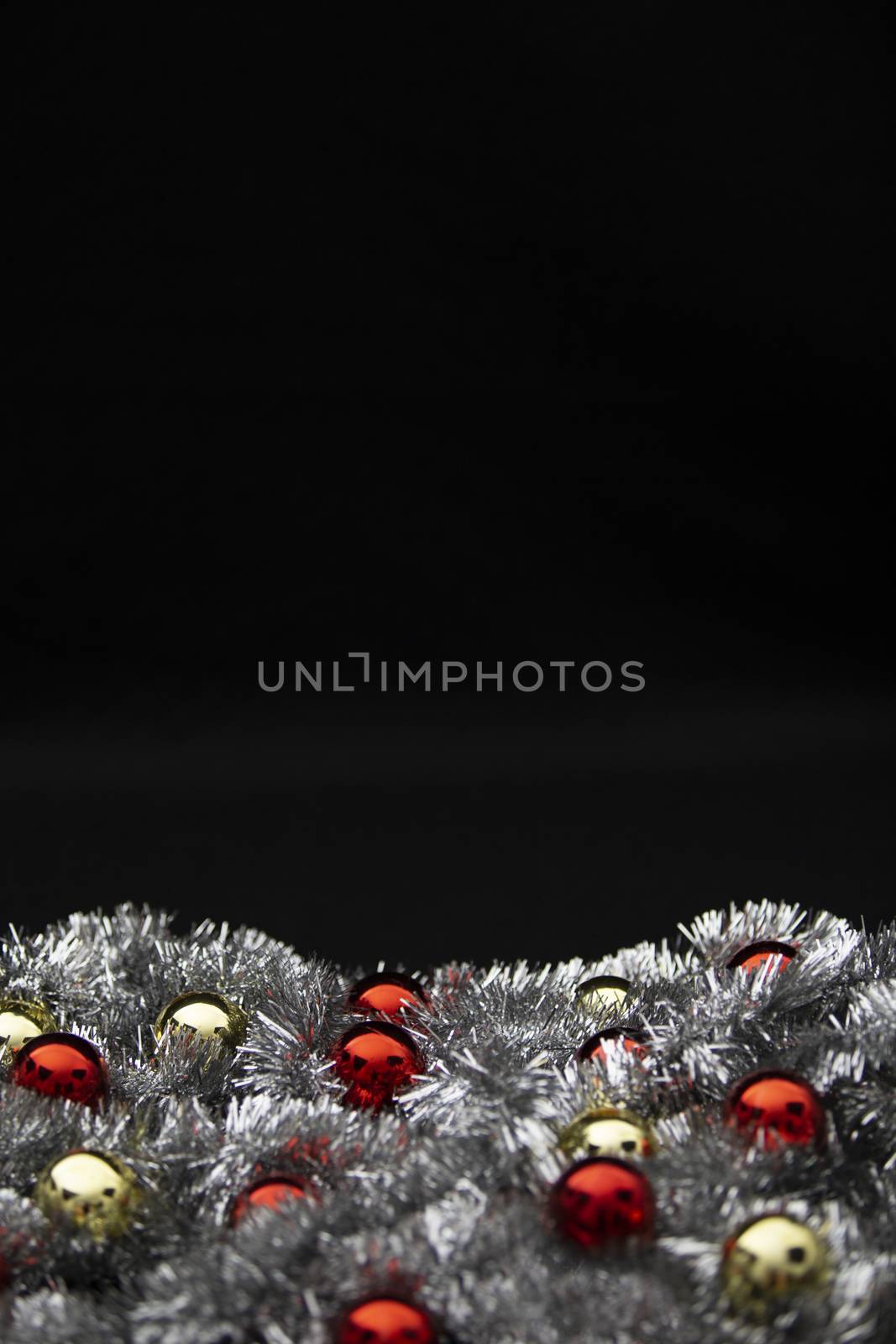 Christmas vertical copy space with red and golden bright baubles in silver decorative chain garland on black background with bokeh effect by robbyfontanesi