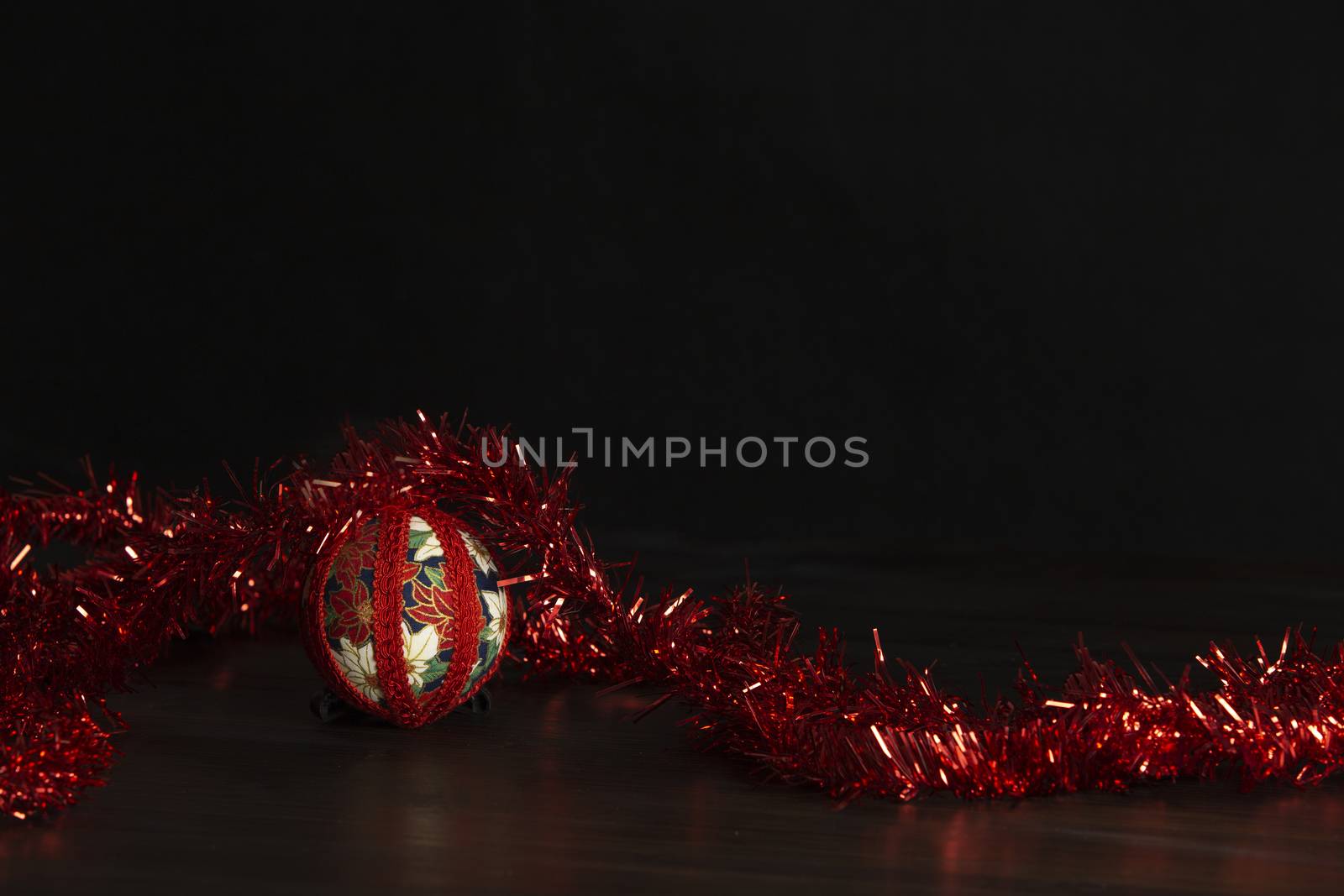 Dark wood Christmas copy space: decoupage christmas isolated ball close up with red decorative wreath ribbon in black background