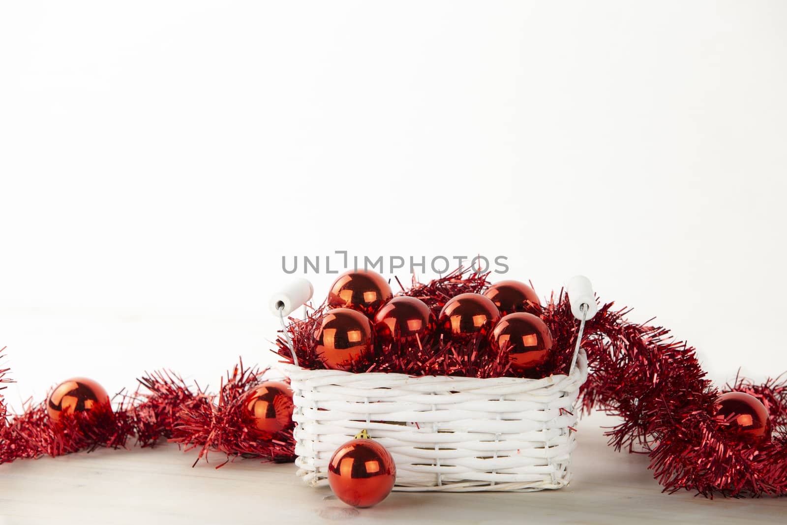 Low angle Christmas copy space: little shabby white basket full of red Christmas baubles with red decorative wreath on light wooden table and white background