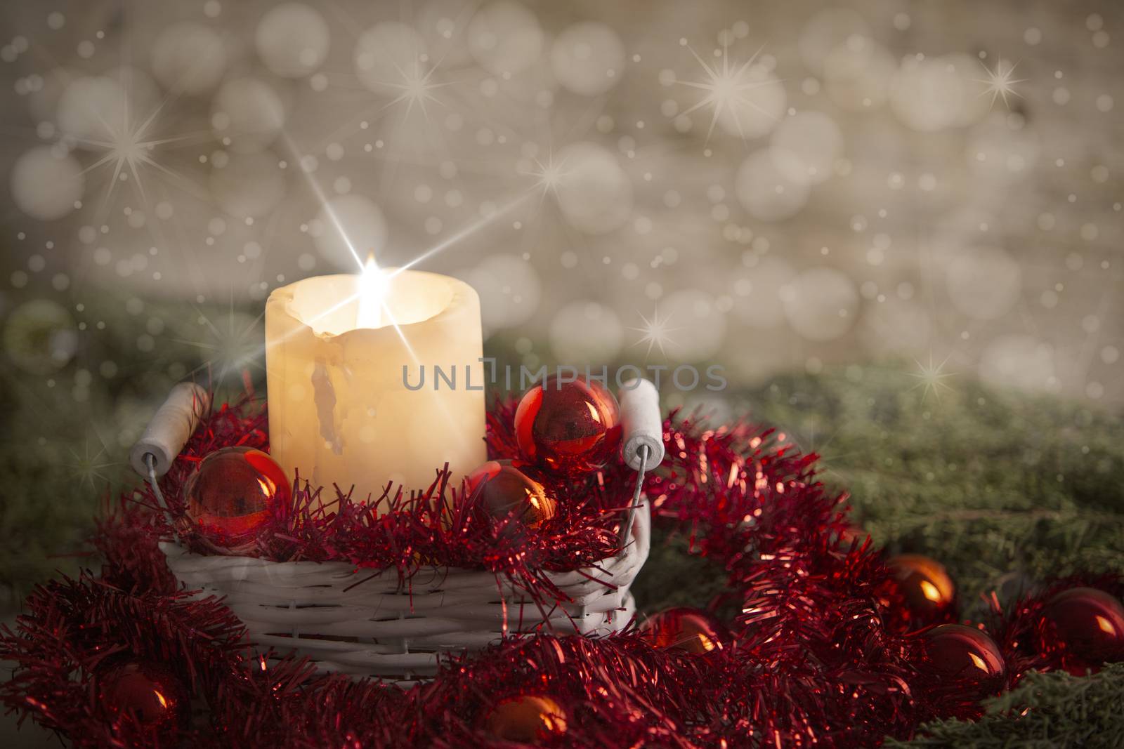 Christmas concept: a lit candle lit with cross screen stars effect in a white shabby basket with red Christmas baubles, red decorative wreath, natural pine branch, wooden background and snow effect
