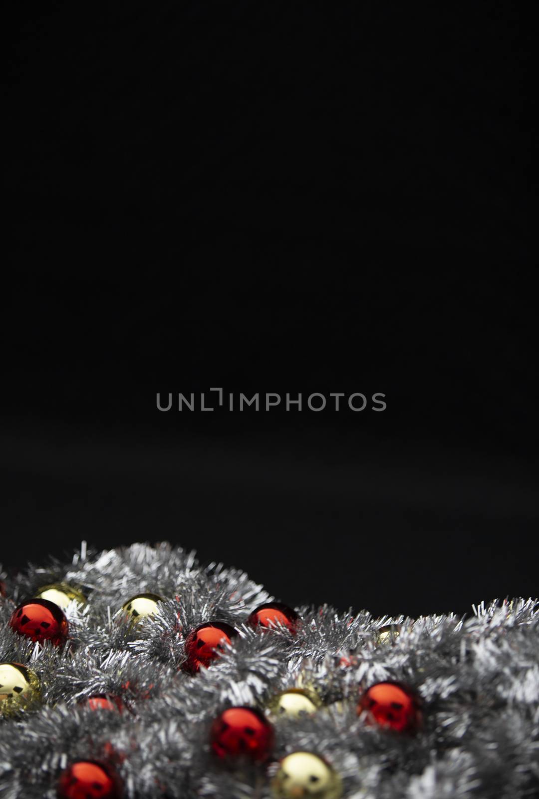 Christmas vertical copy space with red and golden bright baubles in silver decorative chain garland on black background with bokeh effect
