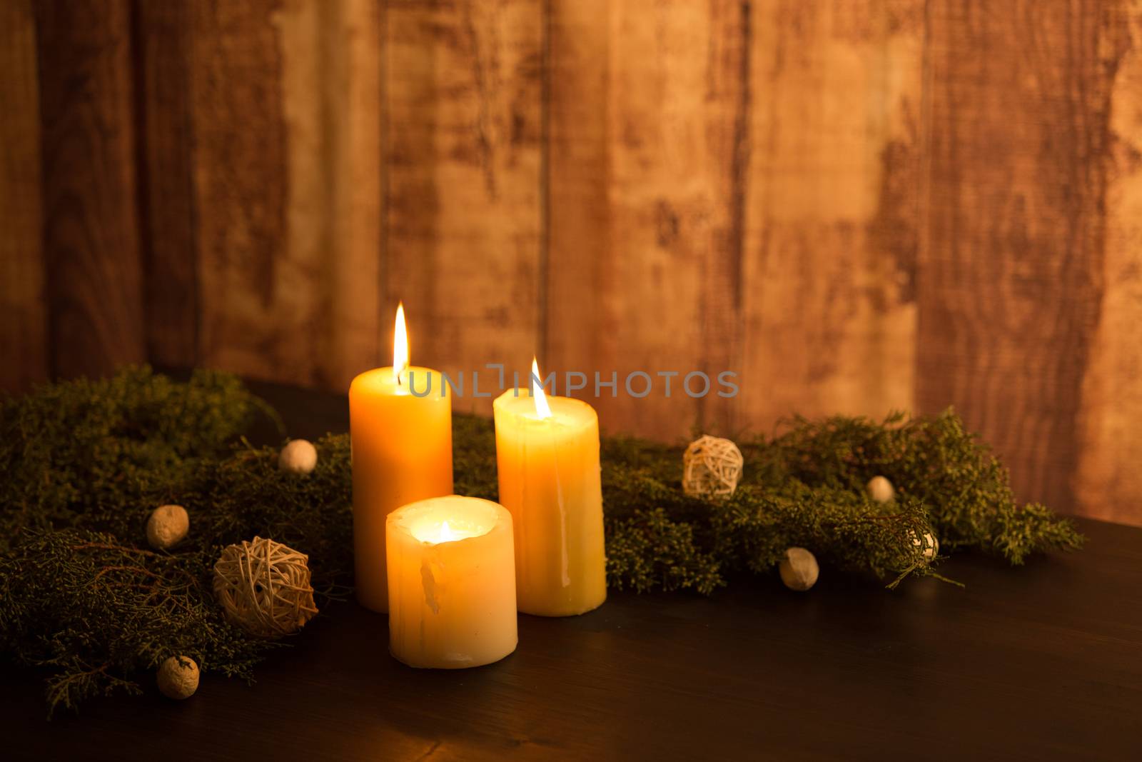 MInimal Christmas concept: three lit candle on a dark wood table and rustic wood ambient with pine branches and white natural decorations by robbyfontanesi