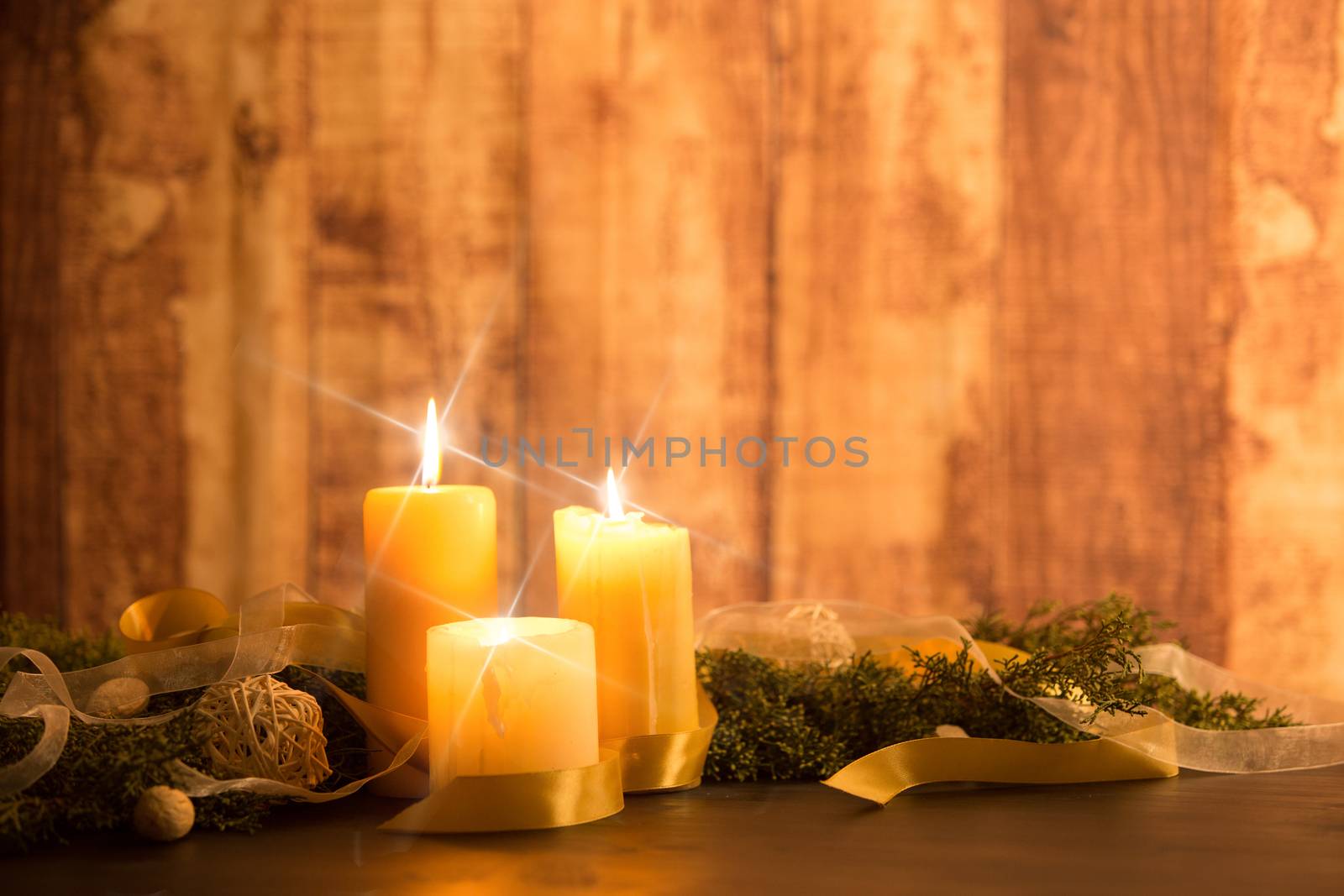 The warmth of the Christmas concept: three candles lit with cross screen stars effect on a dark wooden table with pine branches, natural pine cones with gold satin and white organza ribbons