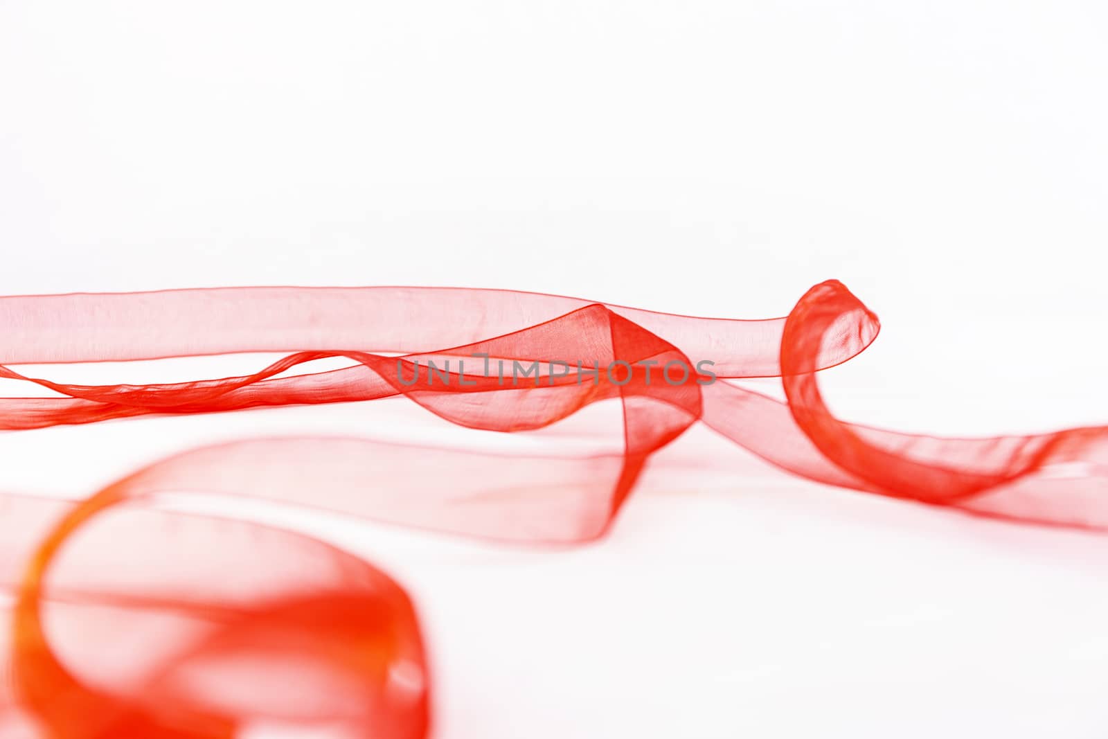Elegant plays of color and transparency with a red organza ribbon that winds over a white background copy space by robbyfontanesi