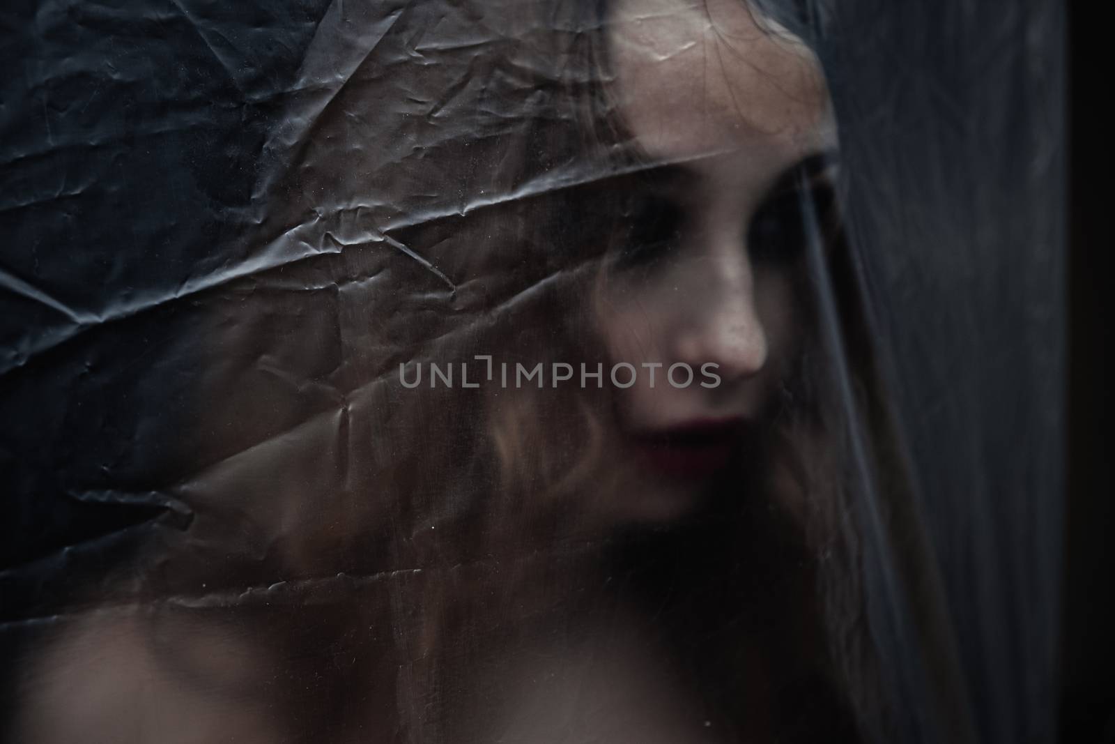 Young beauty sad woman trapped behind a plastic sheet as protection against COVID-19. Nicely fits for book cover