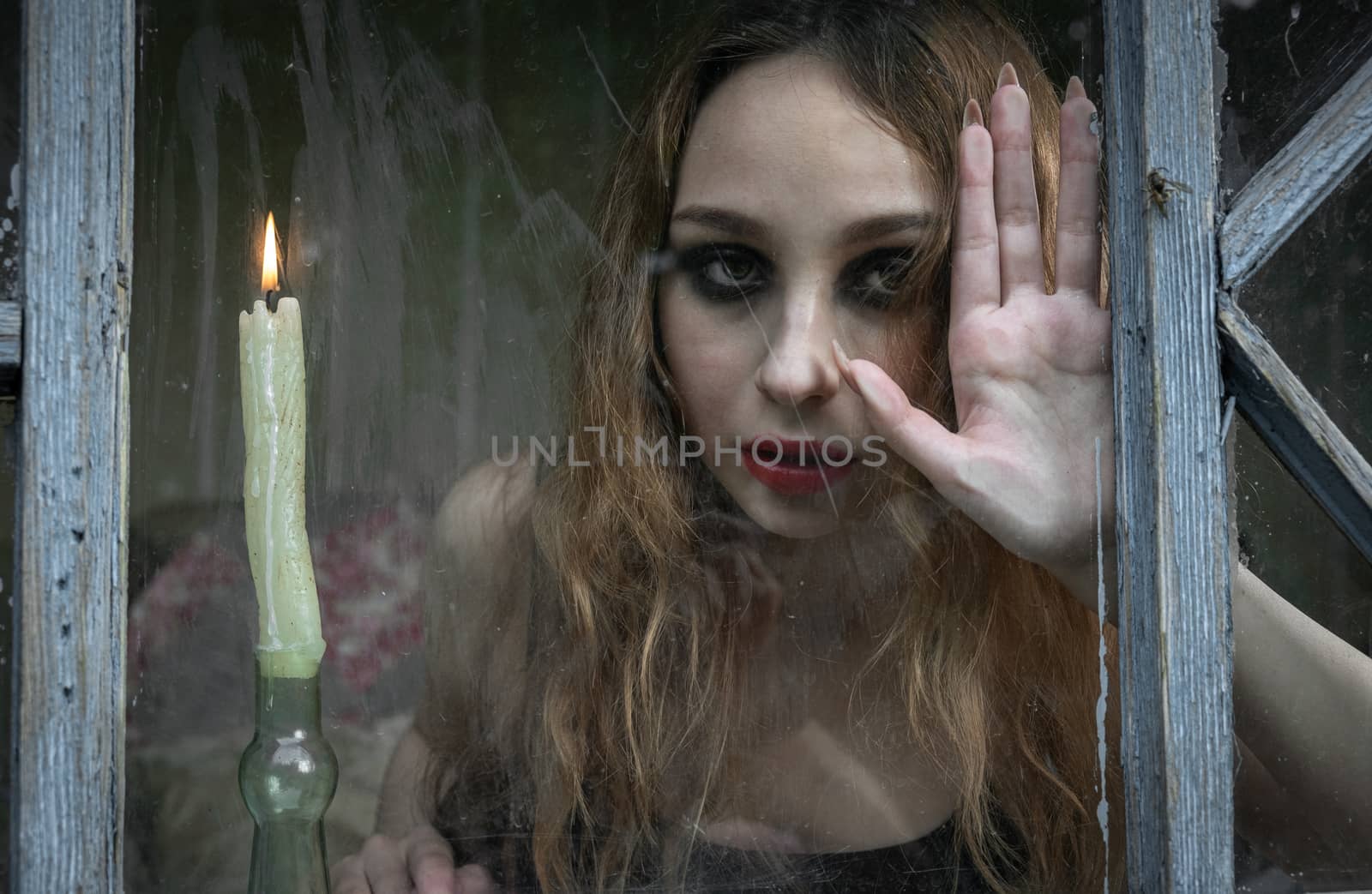 Beautiful sad young girl looking out the window with a candle, good for book cover