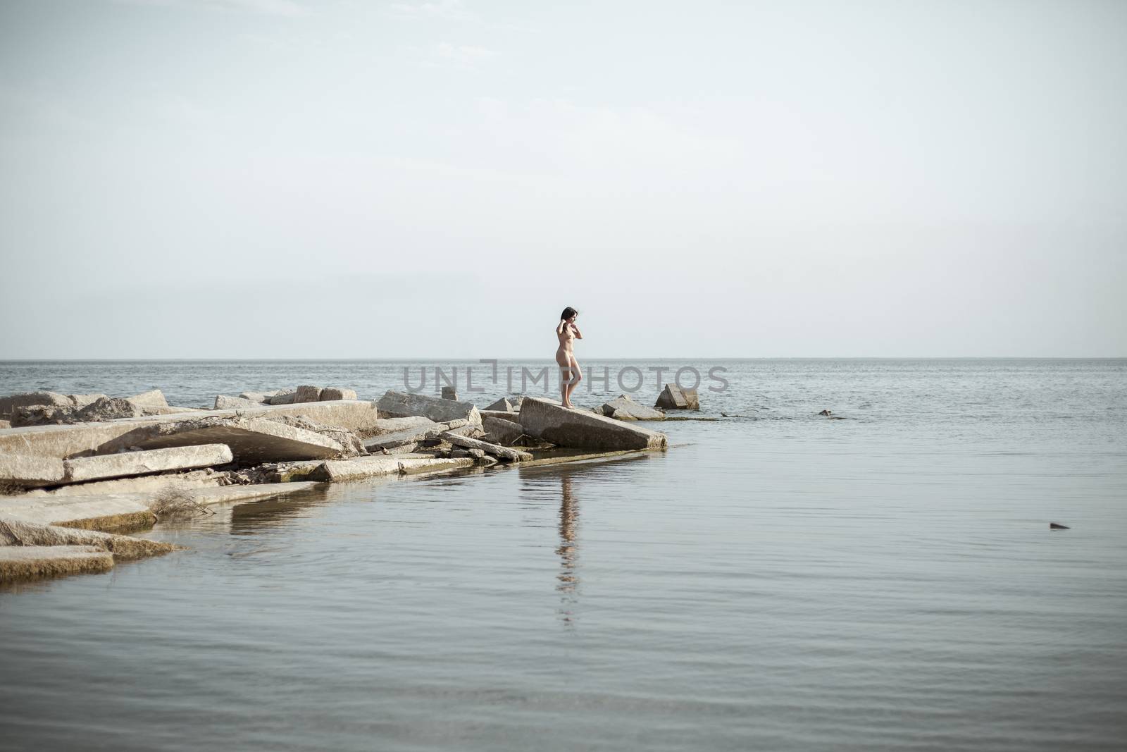 Seascape with naked swimmer girl. Overweight young woman resting in secluded place among coastal rocks