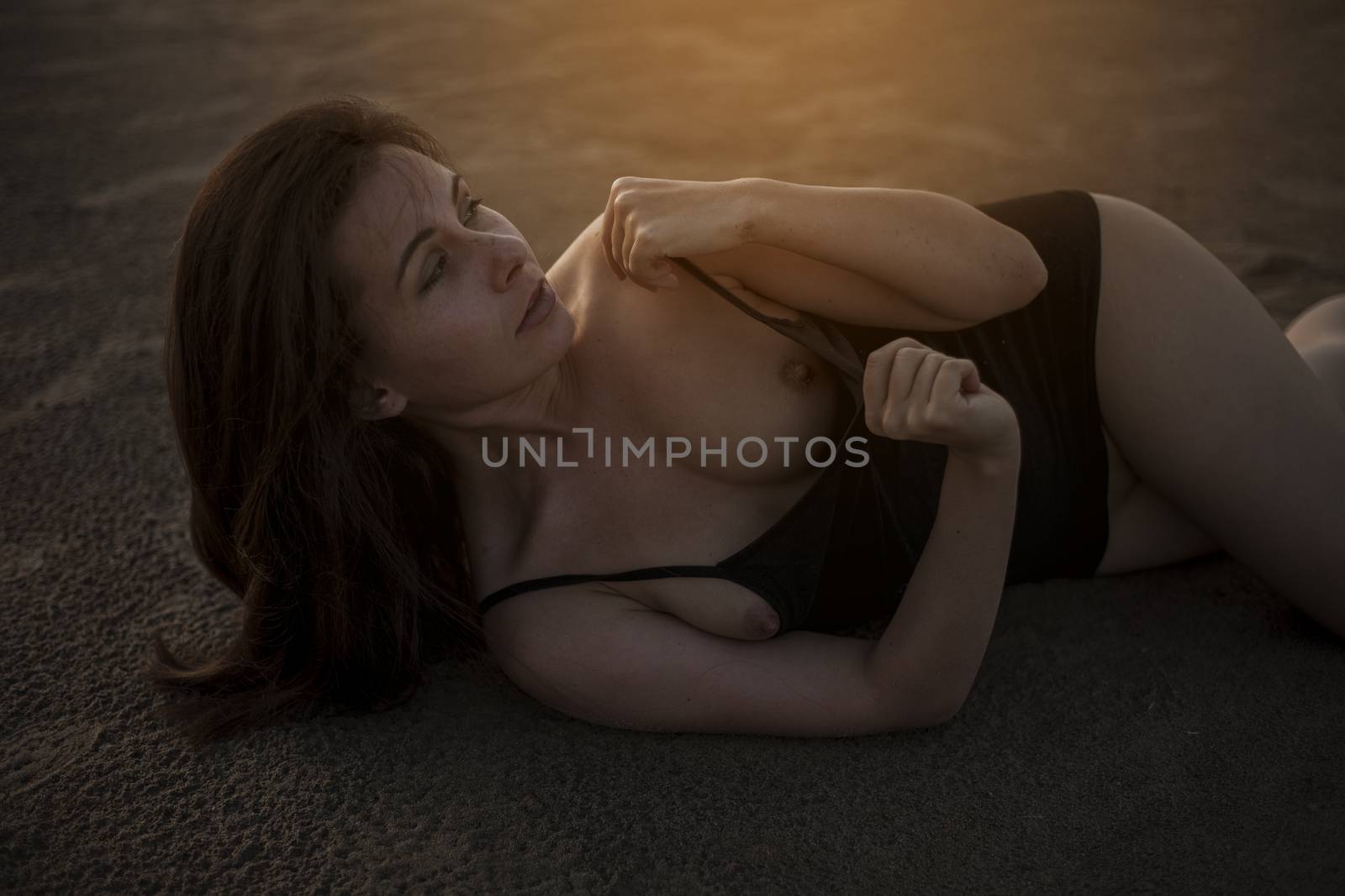 Portrait of a beautiful topless woman with wet hair and body, lying in the sand.