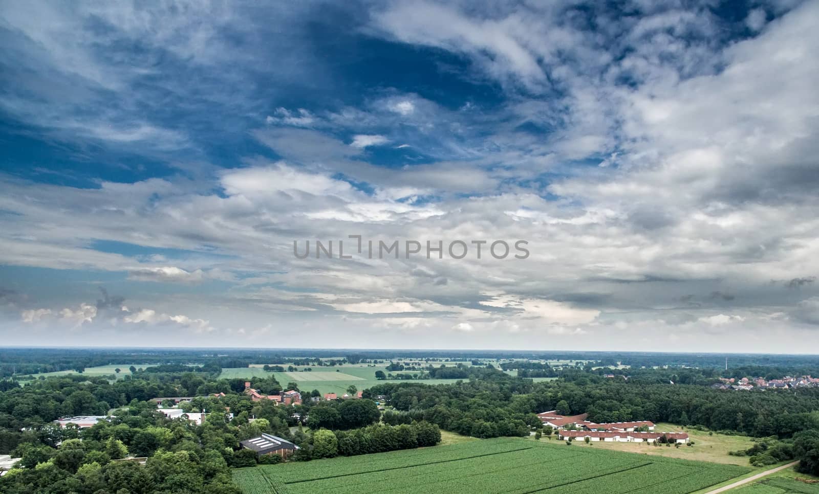 Aerial view of an area of arable land at the edge of a village with connected forest areas and trees along a road in Germany, dramatic sky, made with drone