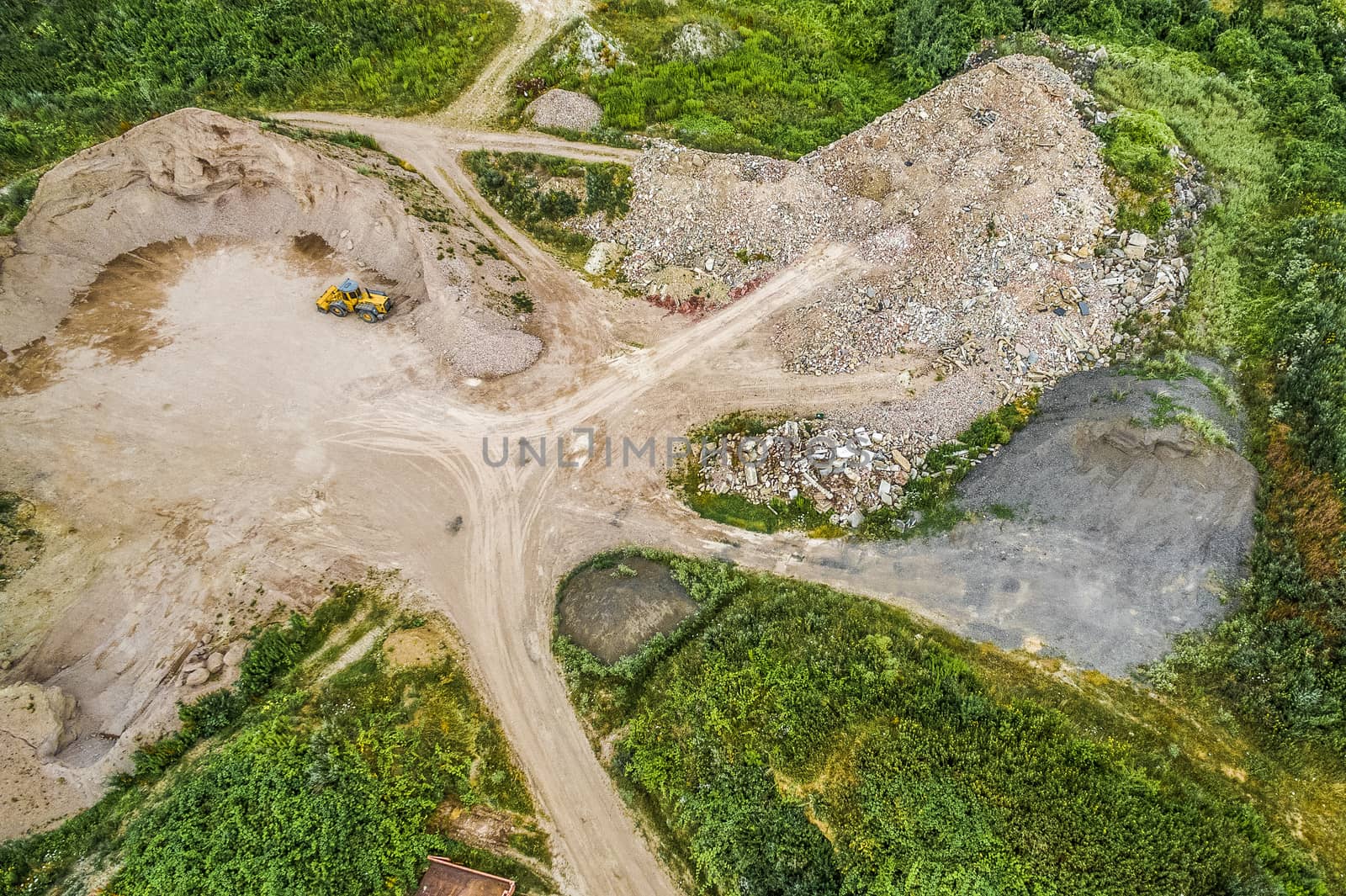 Aerial view of a soil dump and building rubble dump with a sand and gravel heap, several building rubble heaps and a yellow wheel loader, made with drone