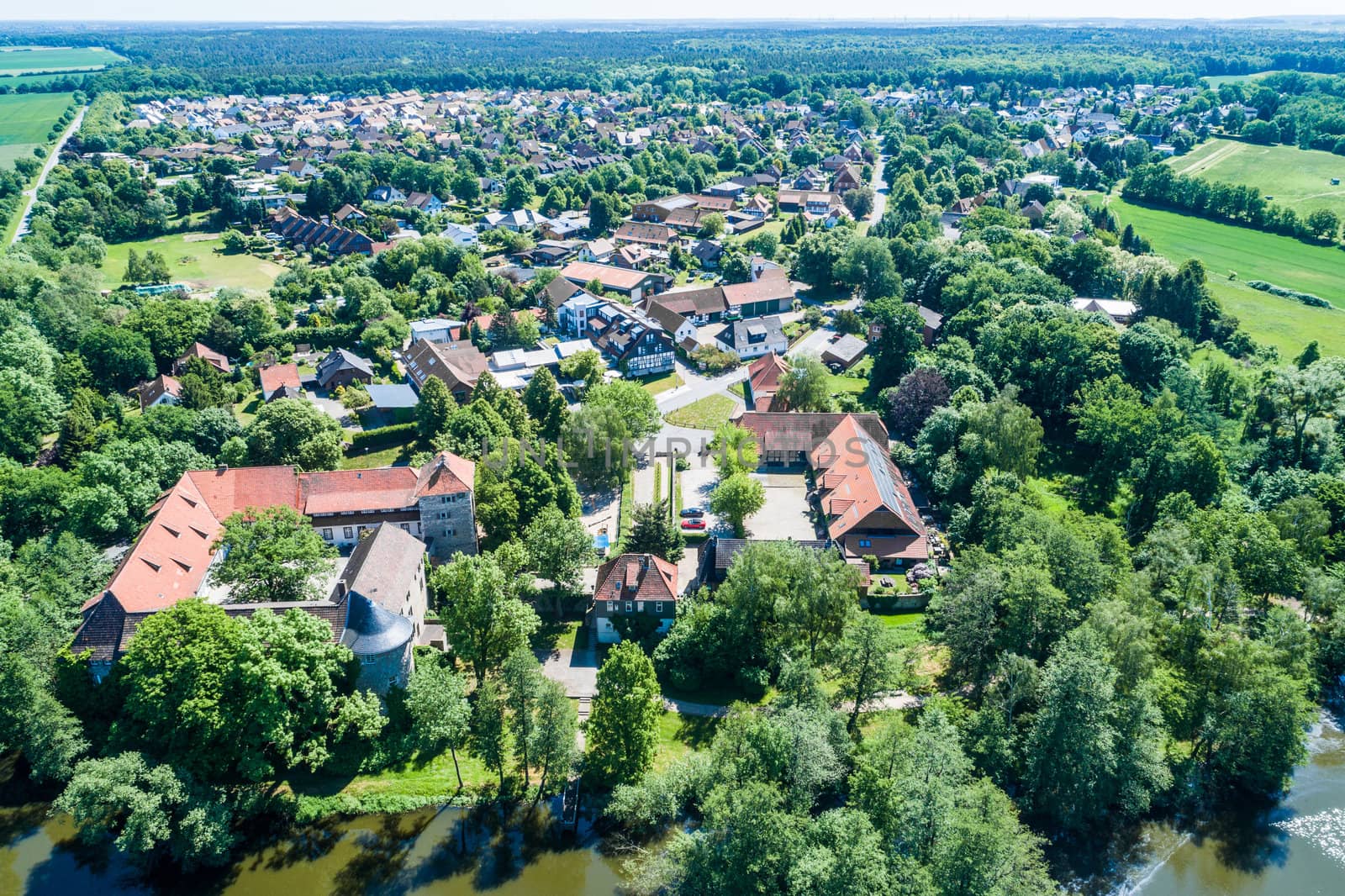 Aerial view of a German village with a small forest, a pond and a moated castle in the foreground by geogif