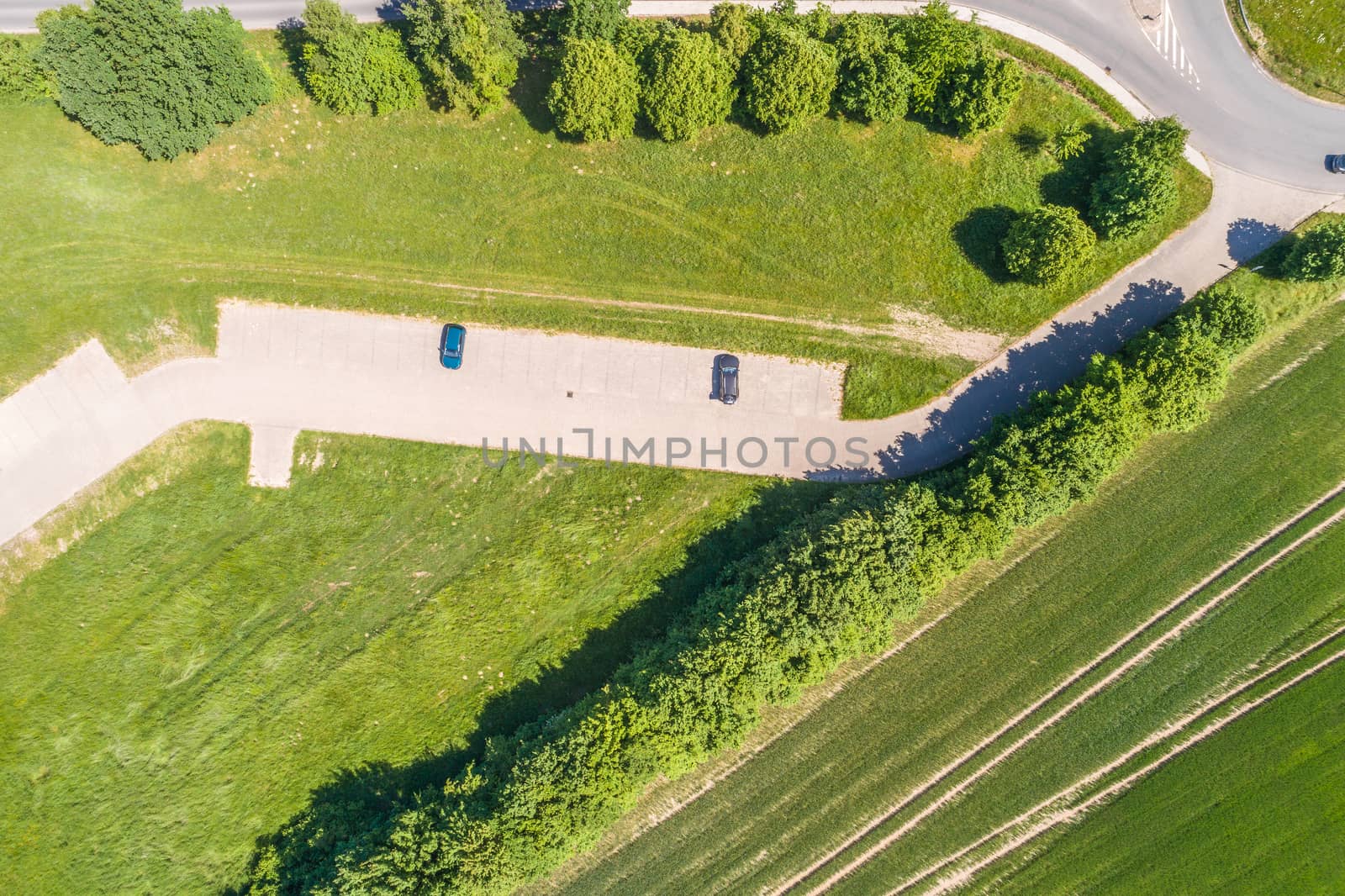 Aerial view of a small parking lot wiping rows of bushes and trees in front of the edge of an arable land, near Wolfsburg