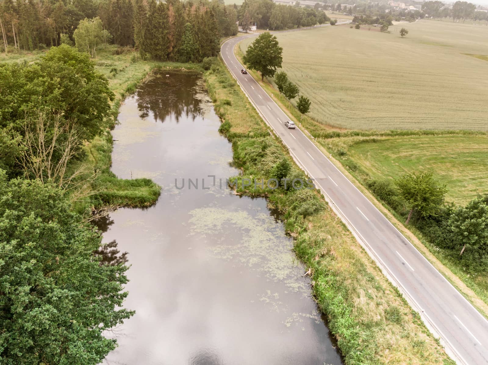 Aerial view of a small pond parallel to a country road in Saxony-Anhalt with fields and forests in the surrounding area by geogif