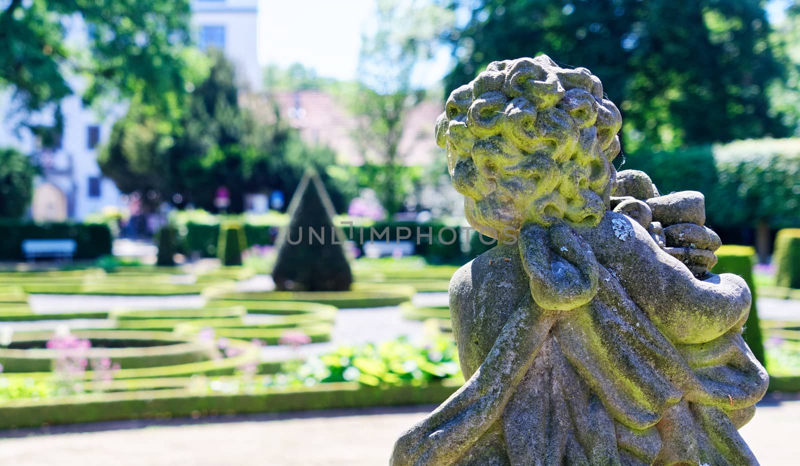 Stone figure of a baroque angel in front of a deliberately blurred background with a baroque garden, germany