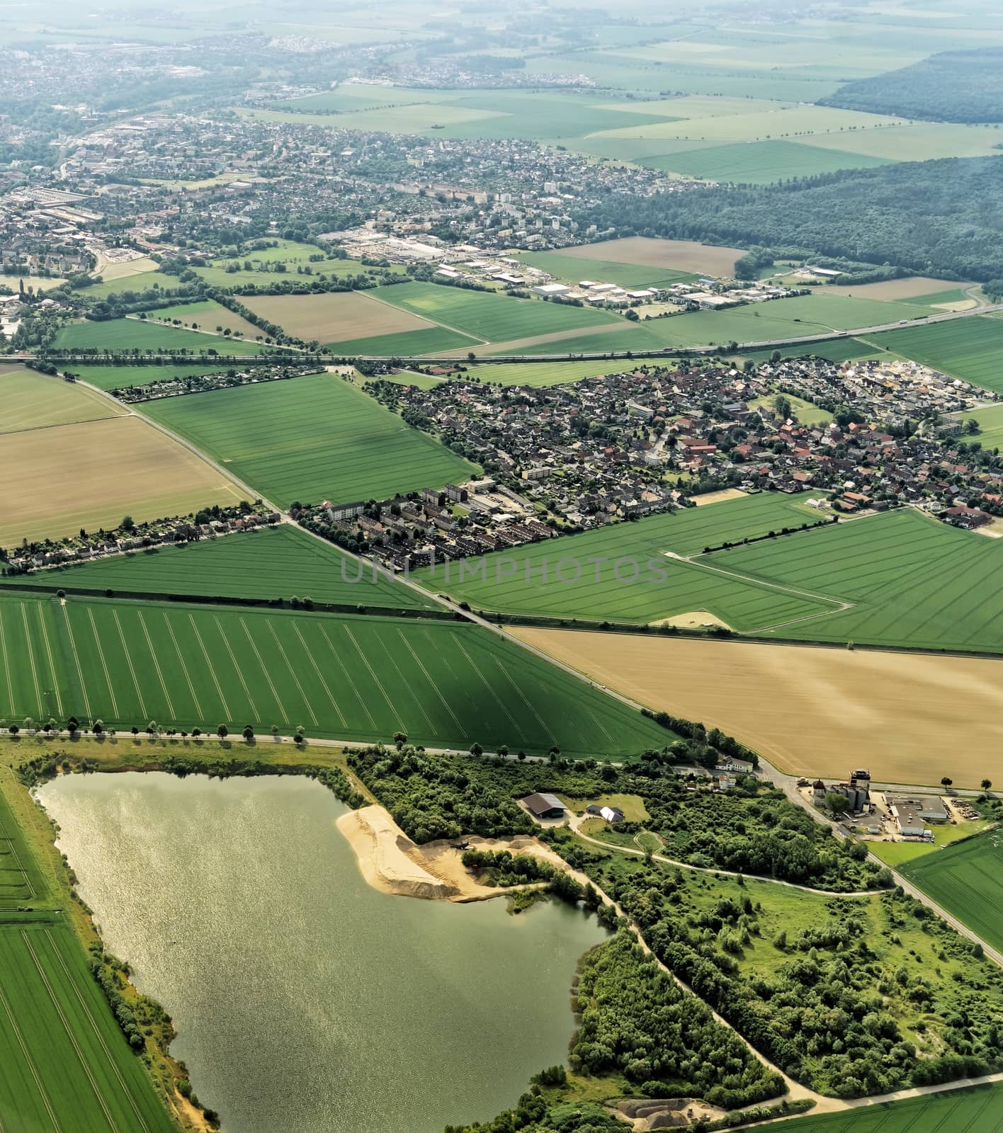 Suburb of Braunschweig, Germany with a water-filled former gravel pit in the foreground, village structure with fields and meadows, aerial photo by geogif