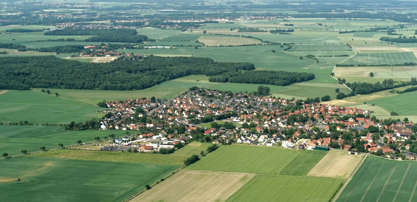 Aerial view from a small airplane from a village near Braunschweig with fields, meadows, farmland and small forests in the area, Germany